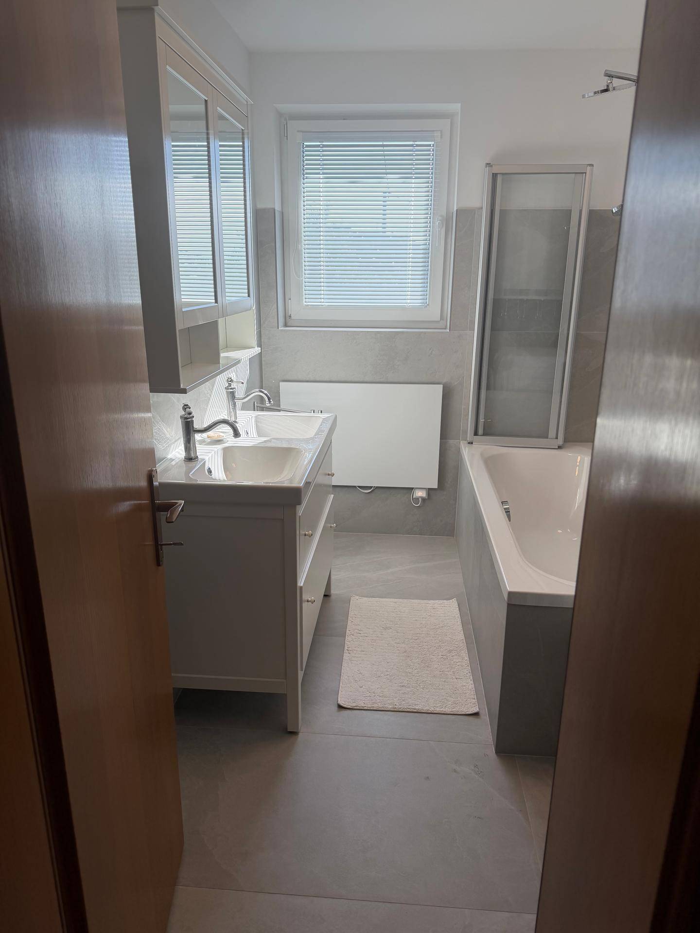 Modernes Badezimmer mit Doppelwaschbecken, Badewanne und grauen Fliesen.