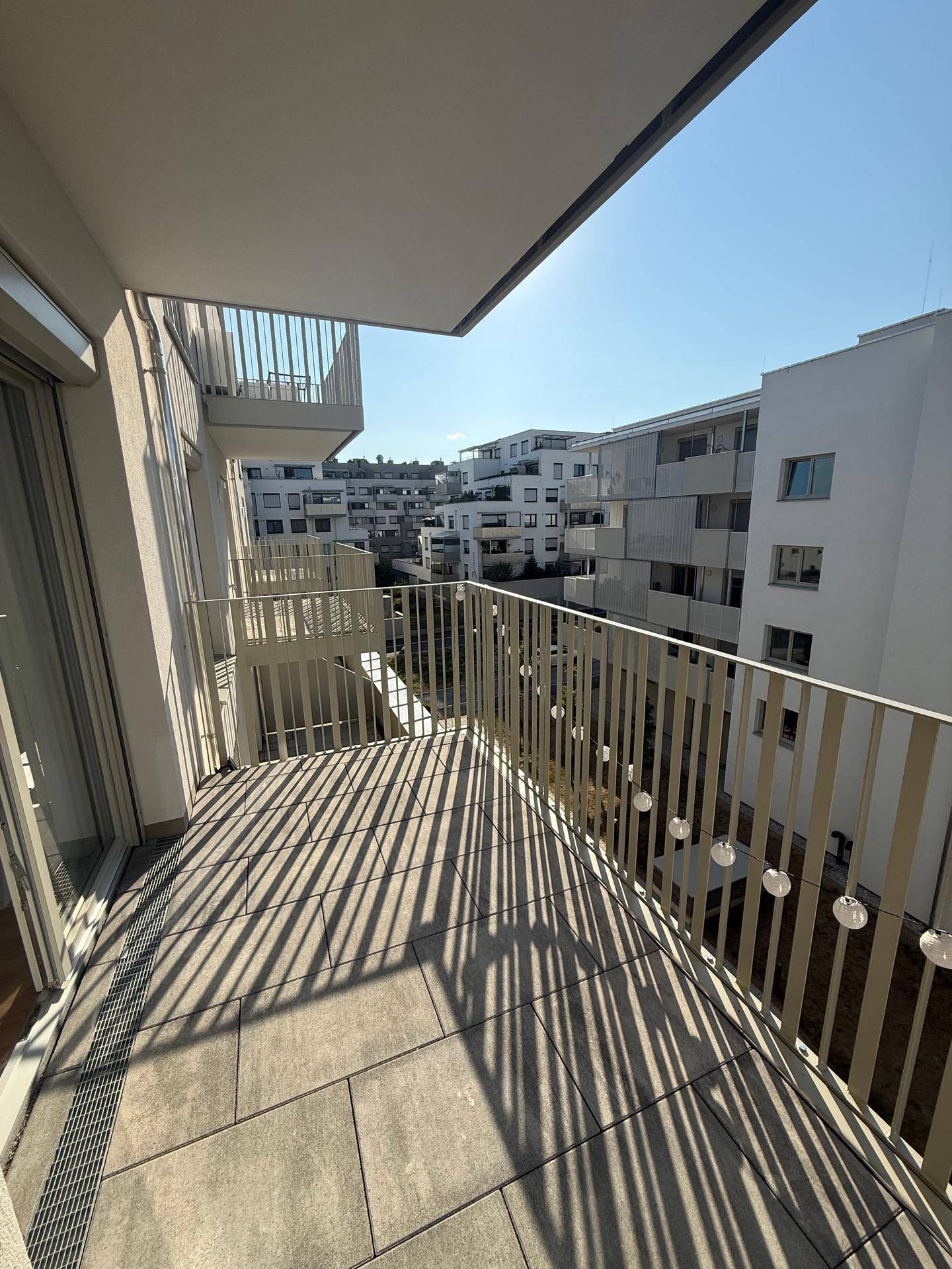 Sonniger Balkon mit Fliesenboden und Blick auf moderne Wohngebäude.