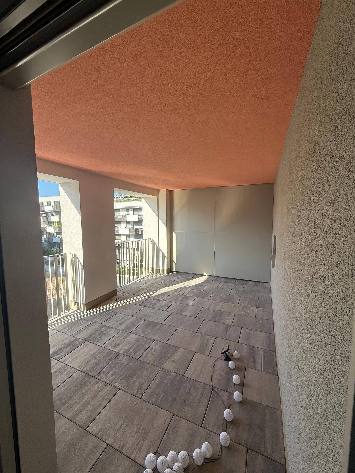 Geräumige überdachte Terrasse mit Fliesenboden und orangefarbener Decke.
