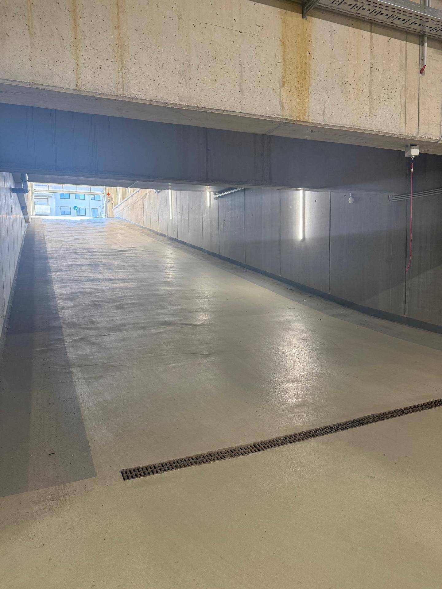 Einfahrt zur Tiefgarage mit Betonwänden und Beleuchtung.