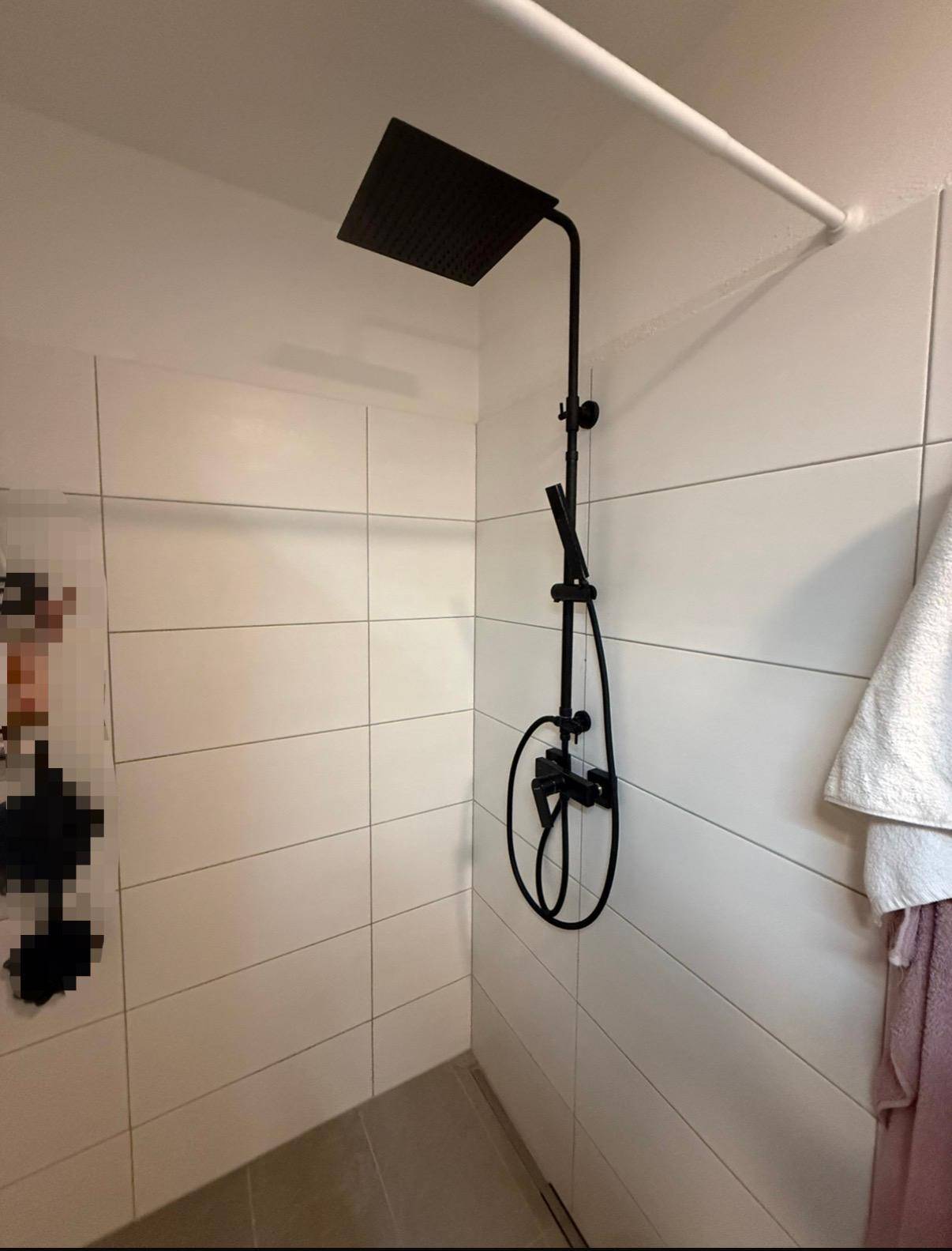 Moderne Dusche mit schwarzem Regenduschkopf und weißen Fliesen.