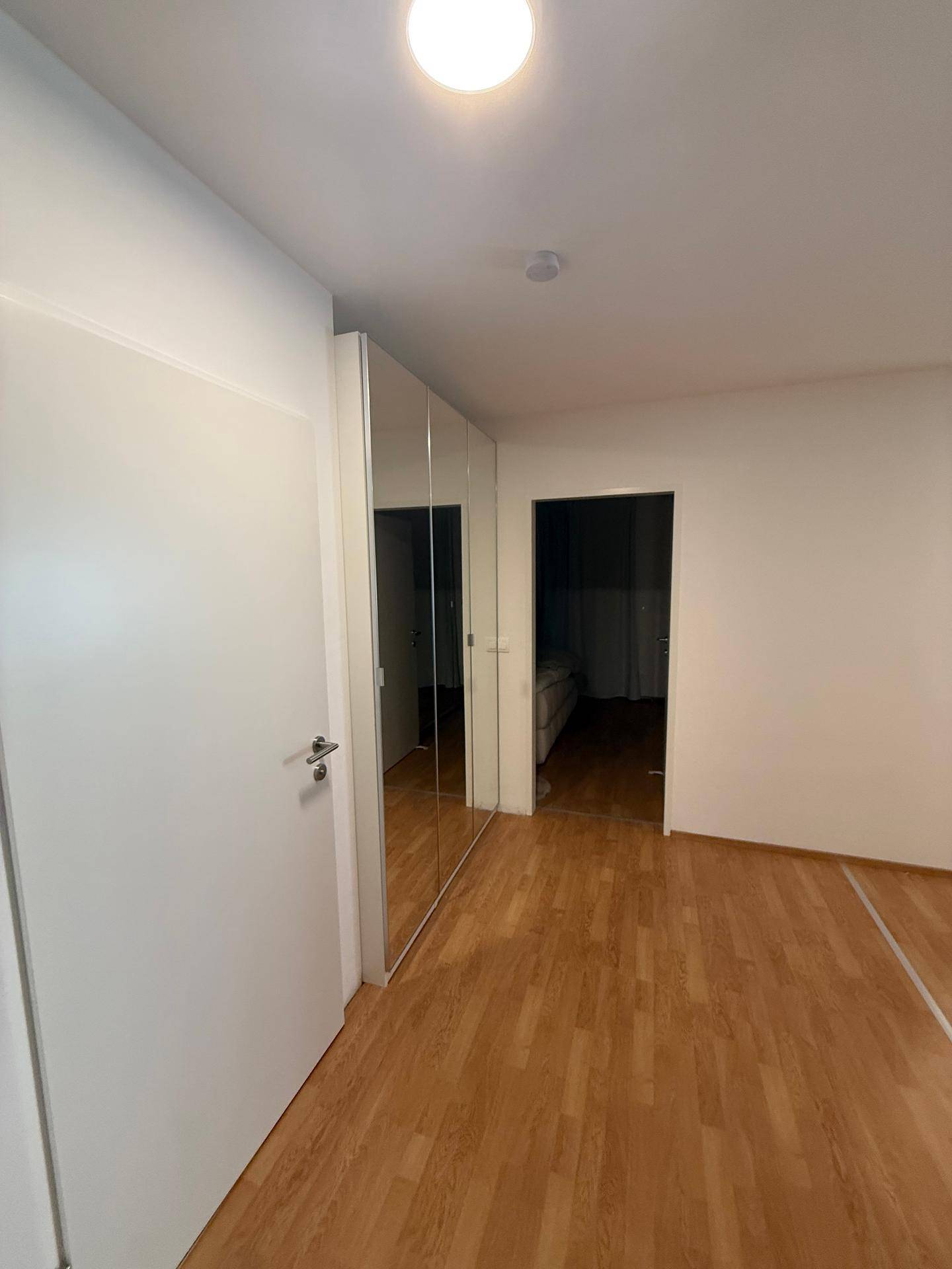 Zimmer mit Laminatboden und großen Spiegelschränken, hell und modern.