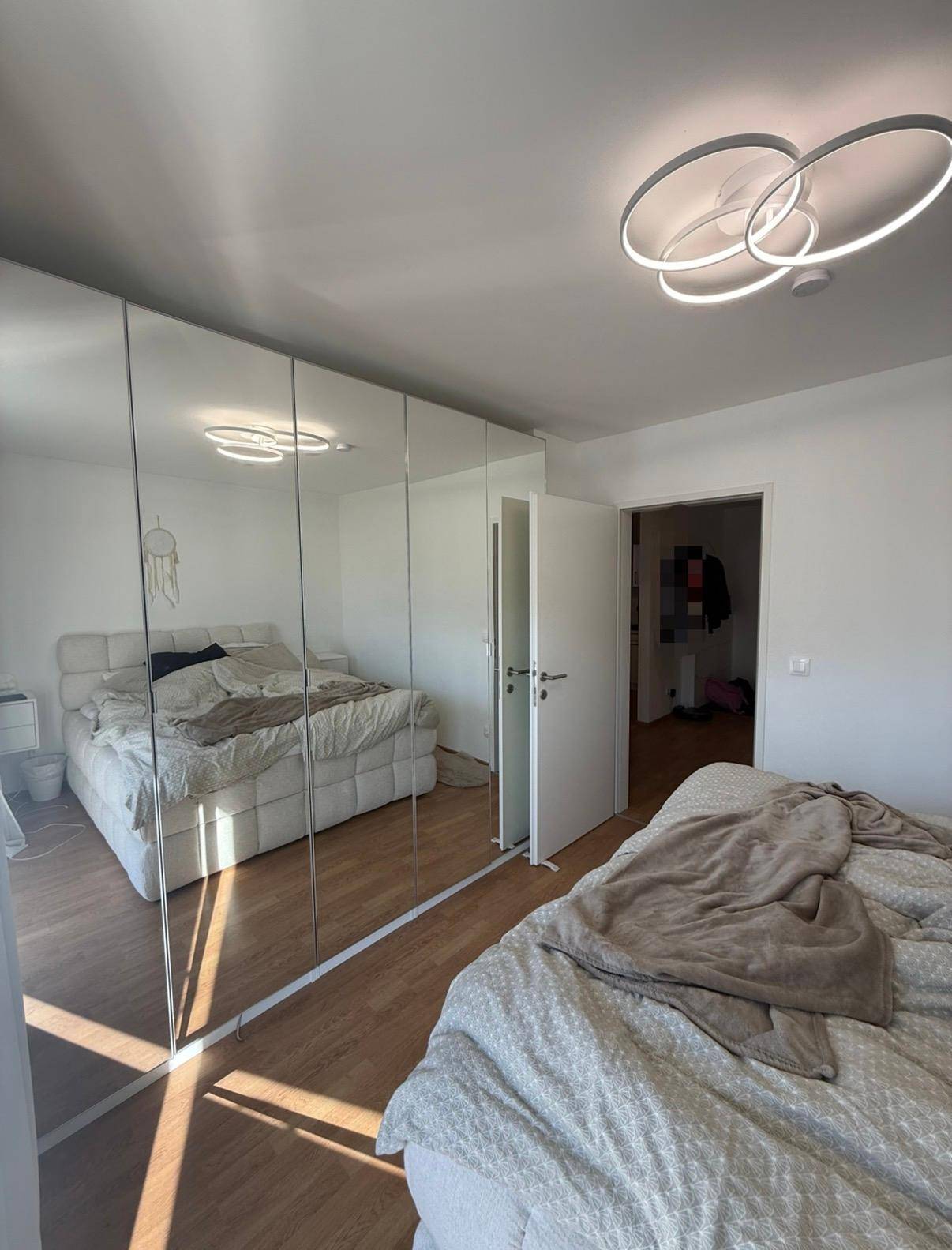 Schlafzimmer mit Spiegelschränken und Blick auf das angrenzende Badezimmer.
