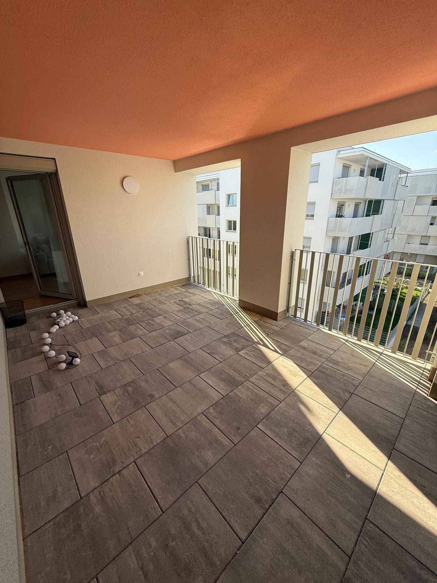 Helle überdachte Terrasse mit Blick auf die umliegenden Wohngebäude.