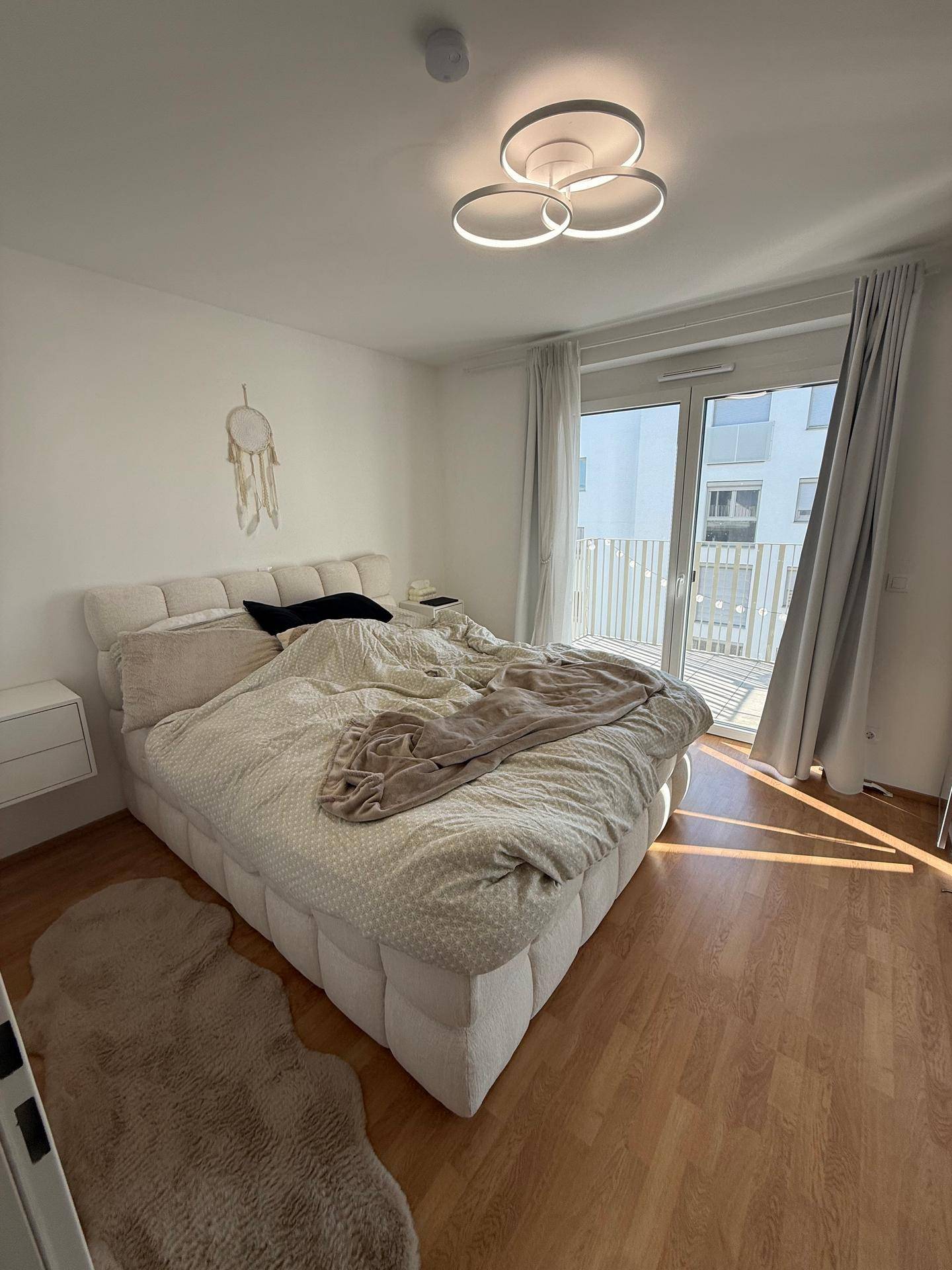 Helles Schlafzimmer mit großem Bett, Laminatboden und Balkonzugang.