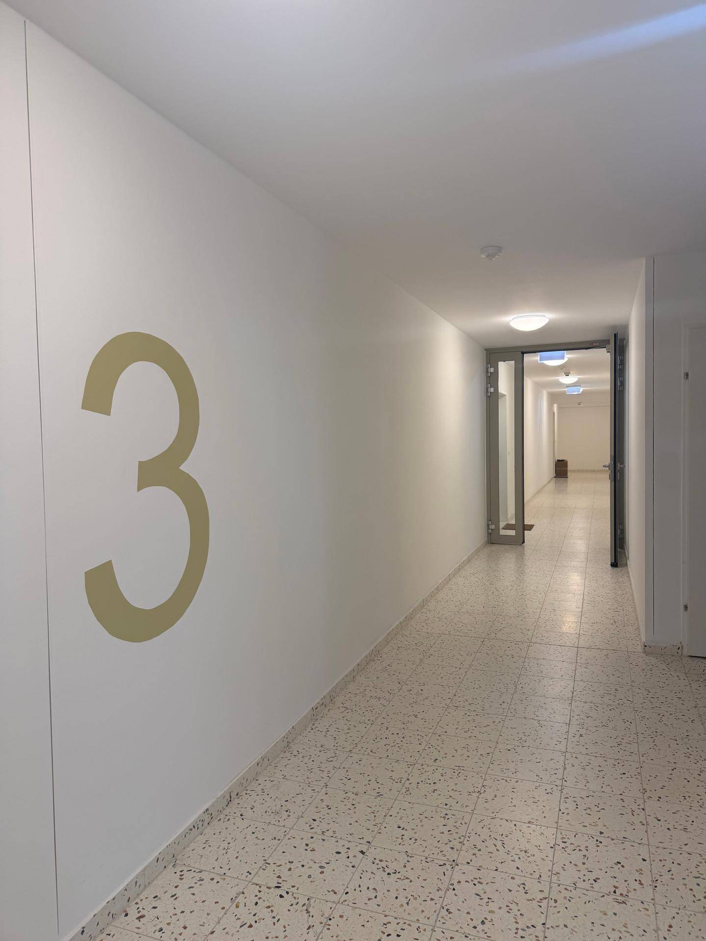 Heller Flur im Gebäude mit Terrazzoboden und moderner Beleuchtung.