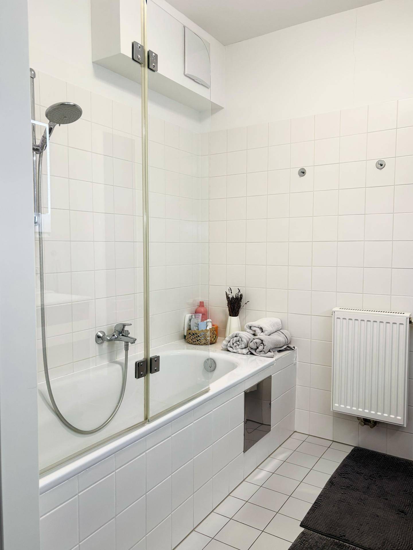 Funktionales Badezimmer mit Badewanne, integrierter Dusche und weißen Fliesen.