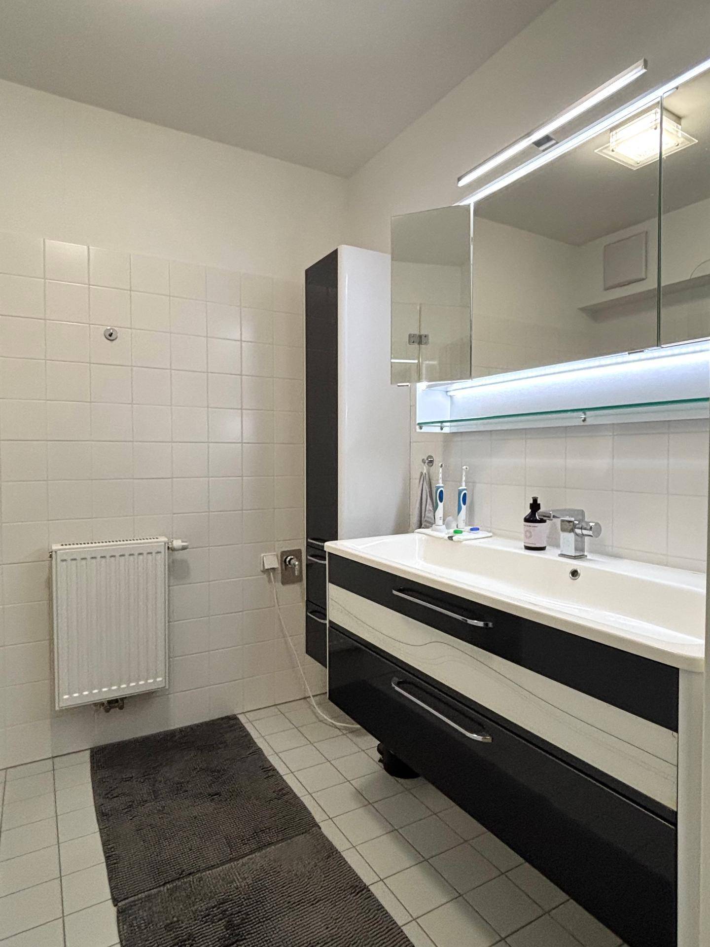 Modernes Badezimmer mit stilvollem Waschtisch, Spiegelschrank und weißen Wandfliesen.