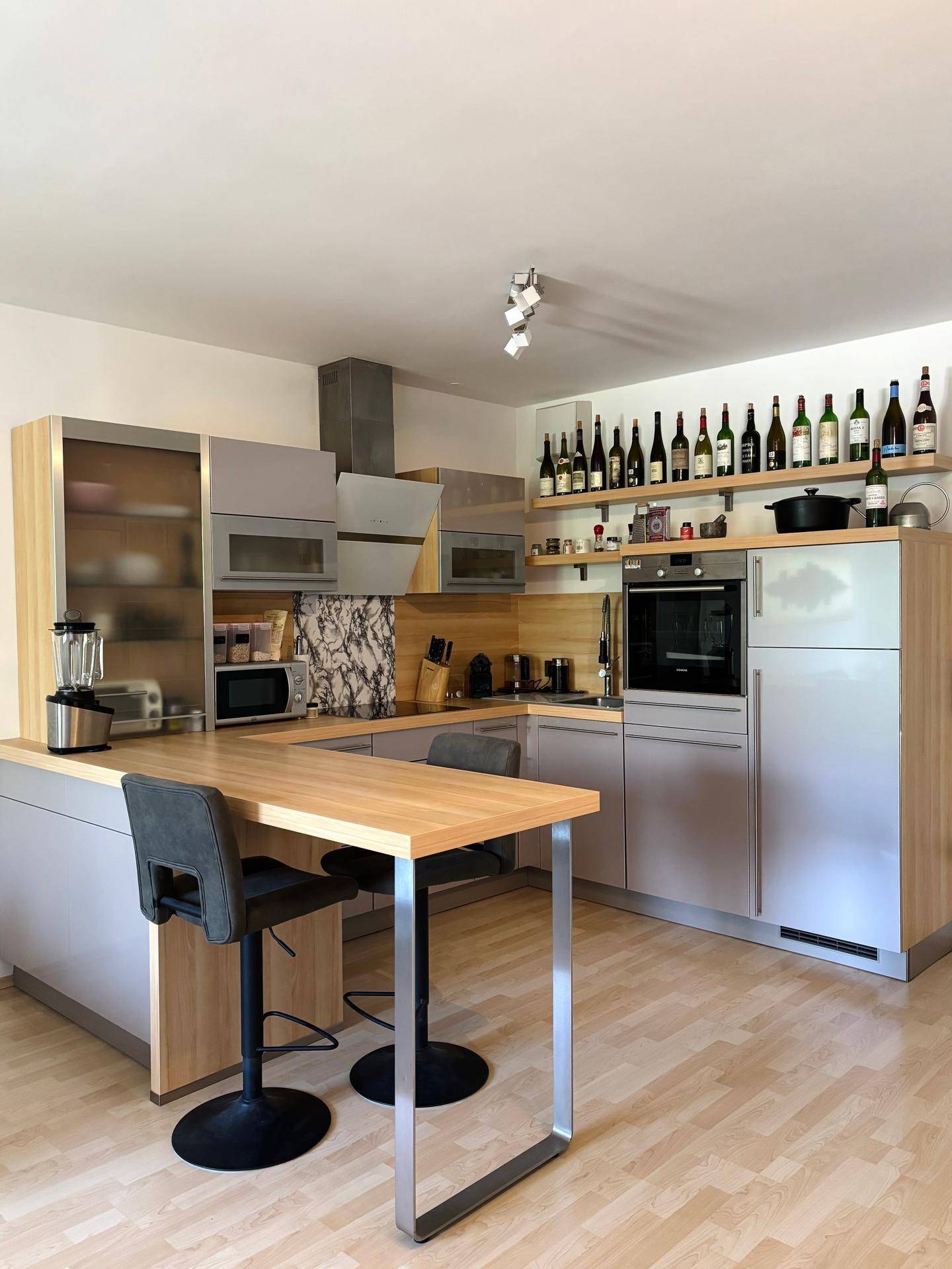 Moderne Einbauküche mit hellgrauen Fronten, Holzarbeitsplatte und praktischer Frühstücksbar.