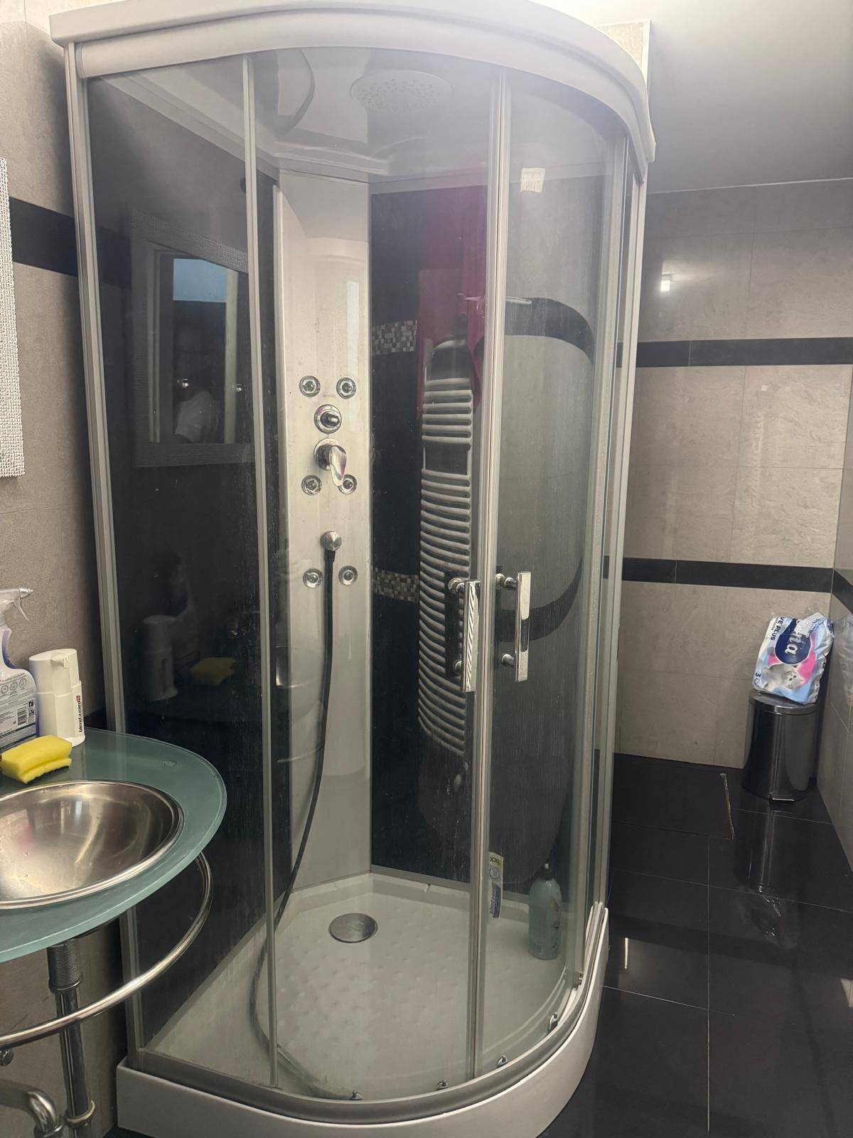 Badezimmer mit moderner Duschkabine, kleinem Waschbecken und dunklen Fliesen an den Wänden.