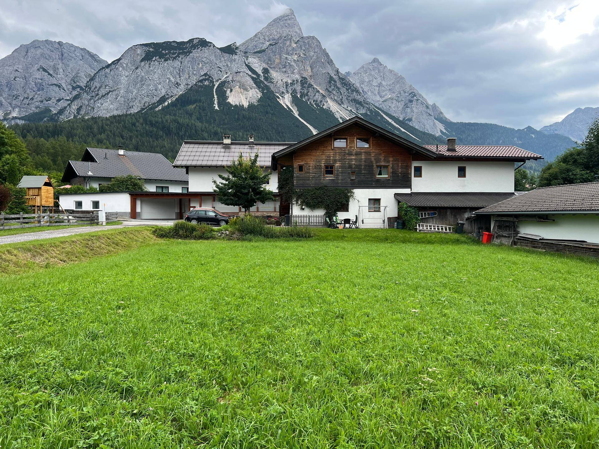 Traditionelles Haus mit Holzelementen und Garage, umgeben von grünen Wiesen und Bergen.