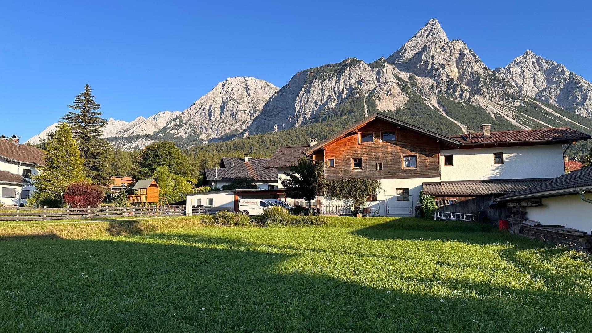 Alpines Haus mit Holzelementen und beeindruckendem Bergblick, umgeben von grünen Wiesen.