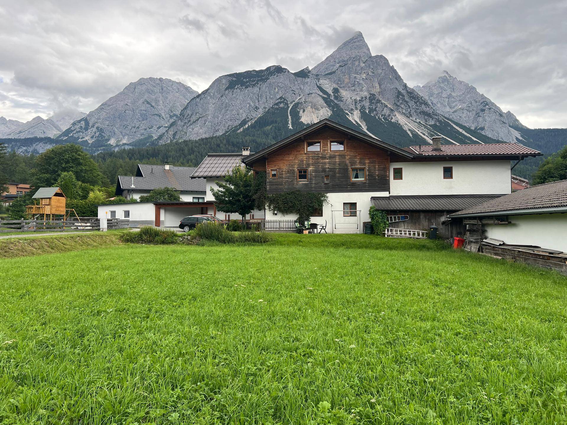 Alpines Haus mit Holzelementen und majestätischem Bergblick unter bewölktem Himmel.