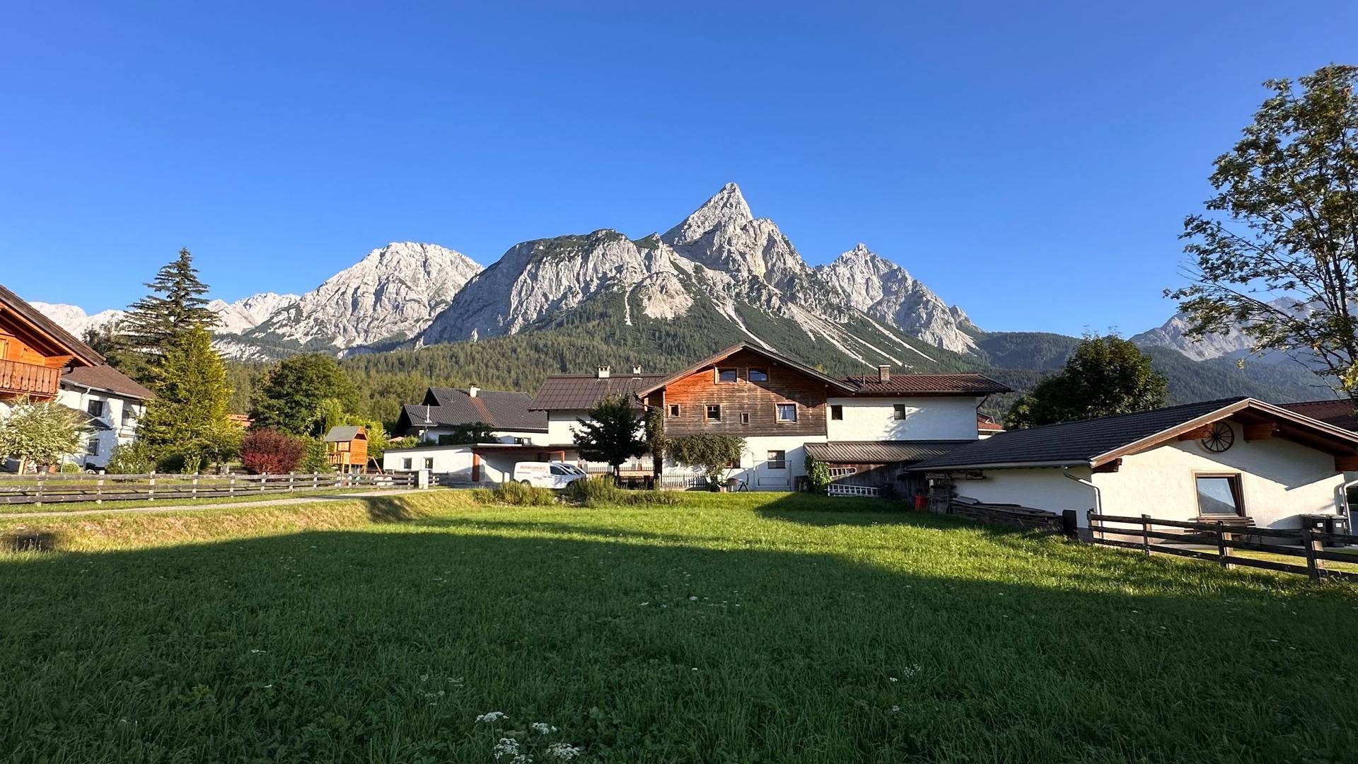 Sonnige Landschaft mit Häusern und einer majestätischen Bergkette, die sich am Horizont erhebt.