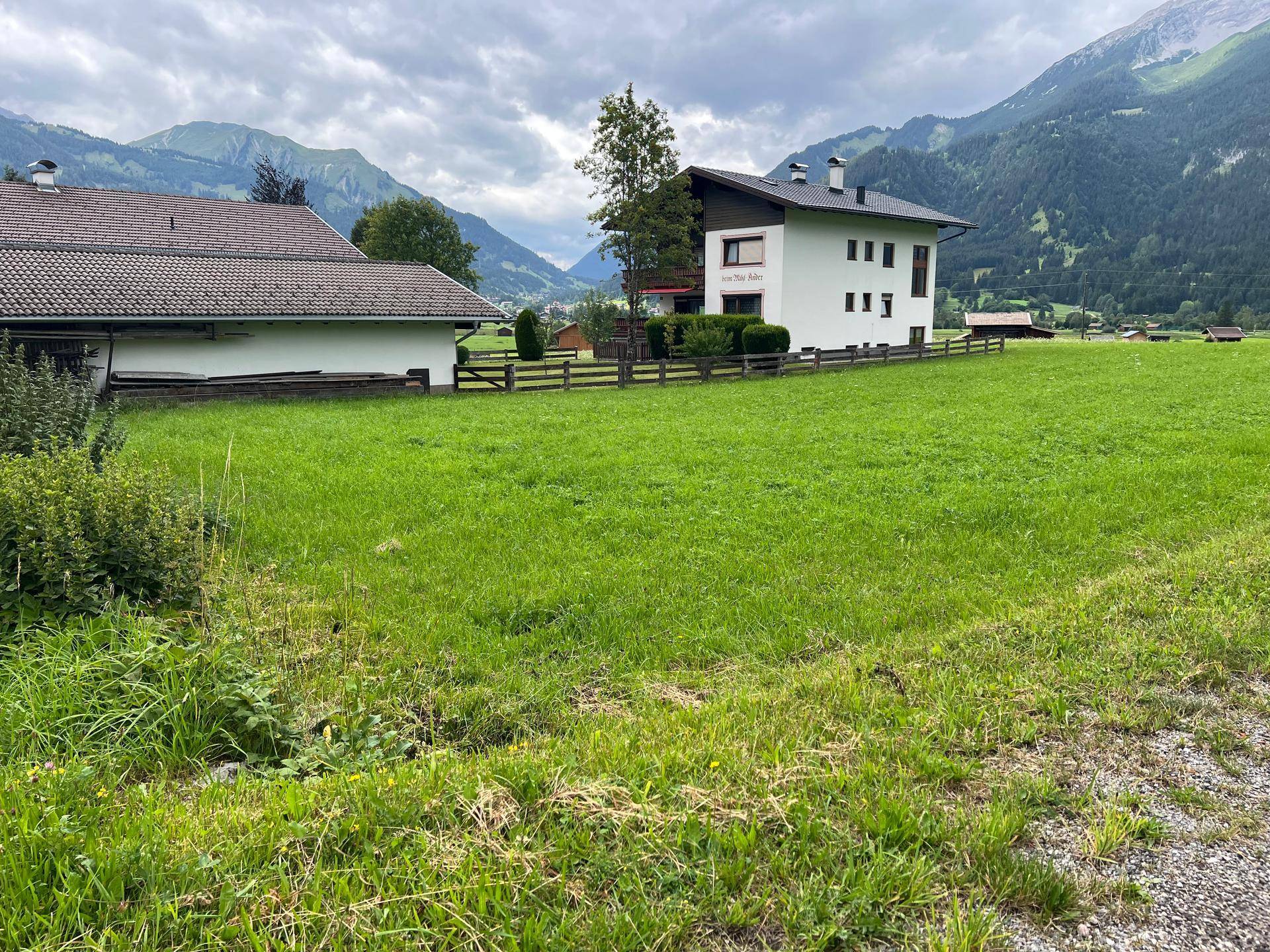 Grüne Wiese vor einem Wohnhaus mit Blick auf die sanften Hügel und Berge in der Ferne.