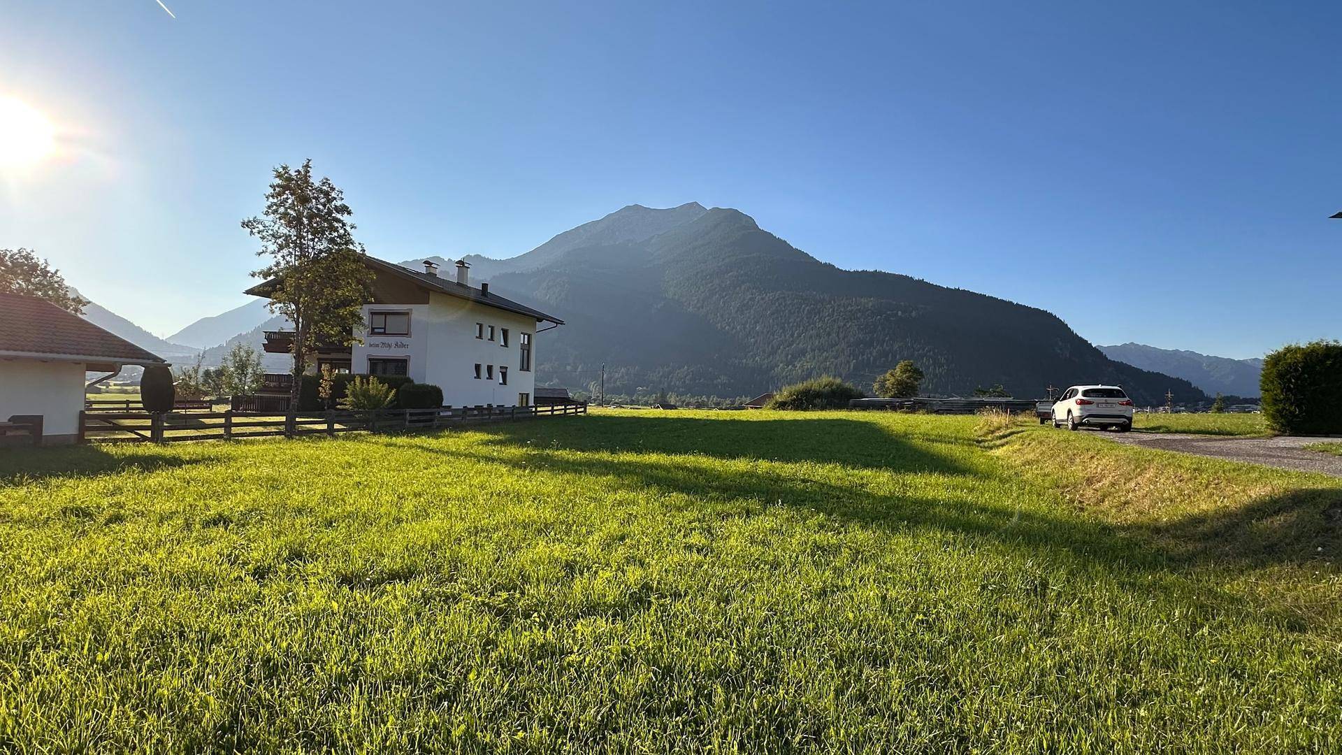 Sonnige Wiese vor einem modernen Wohnhaus mit weitem Blick auf die umliegende Berglandschaft.