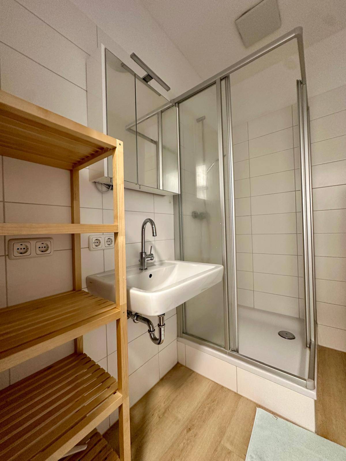 Modernes Badezimmer mit Duschkabine, Einzelwaschbecken und praktischem Holzregal.