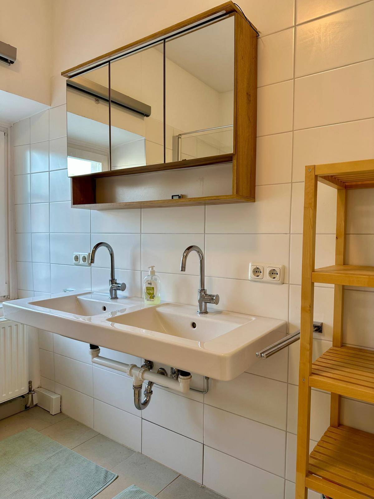 Badezimmer mit Doppelwaschbecken, Spiegelschrank und weißen Fliesen an den Wänden.