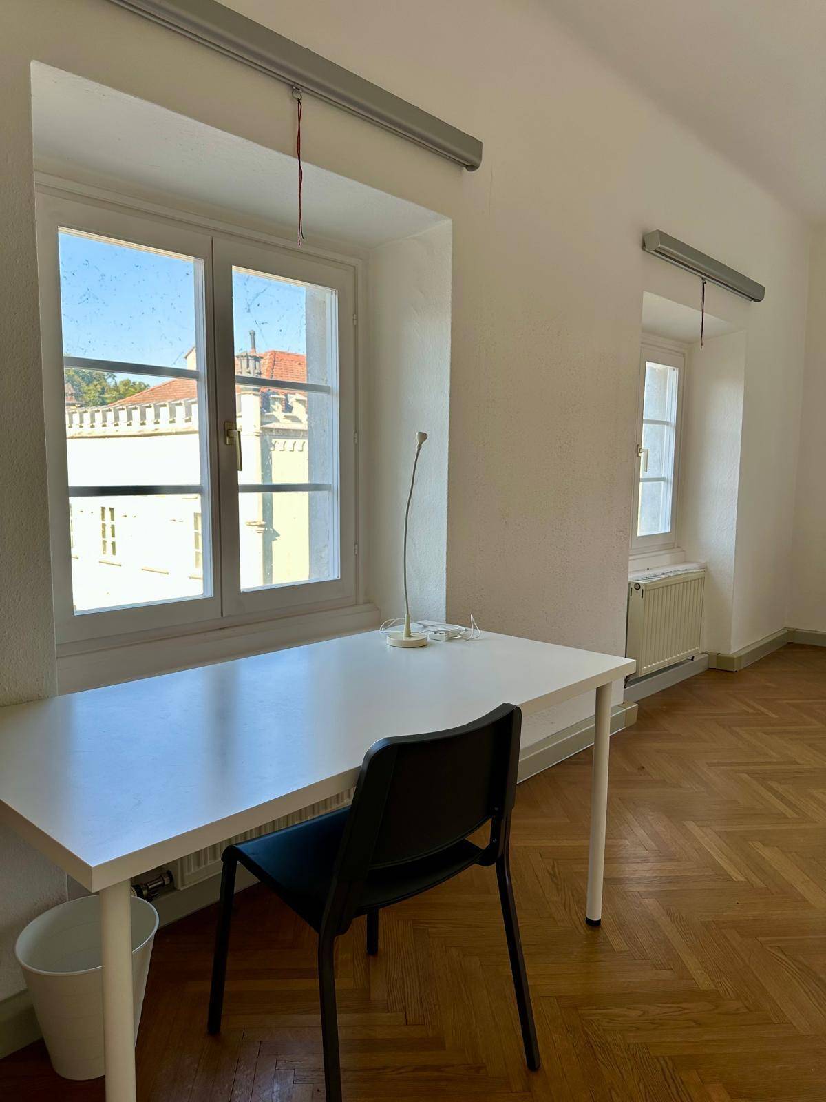 Heller Raum mit Schreibtisch am Fenster und Holzboden, ideal als Schlaf- oder Arbeitszimmer.