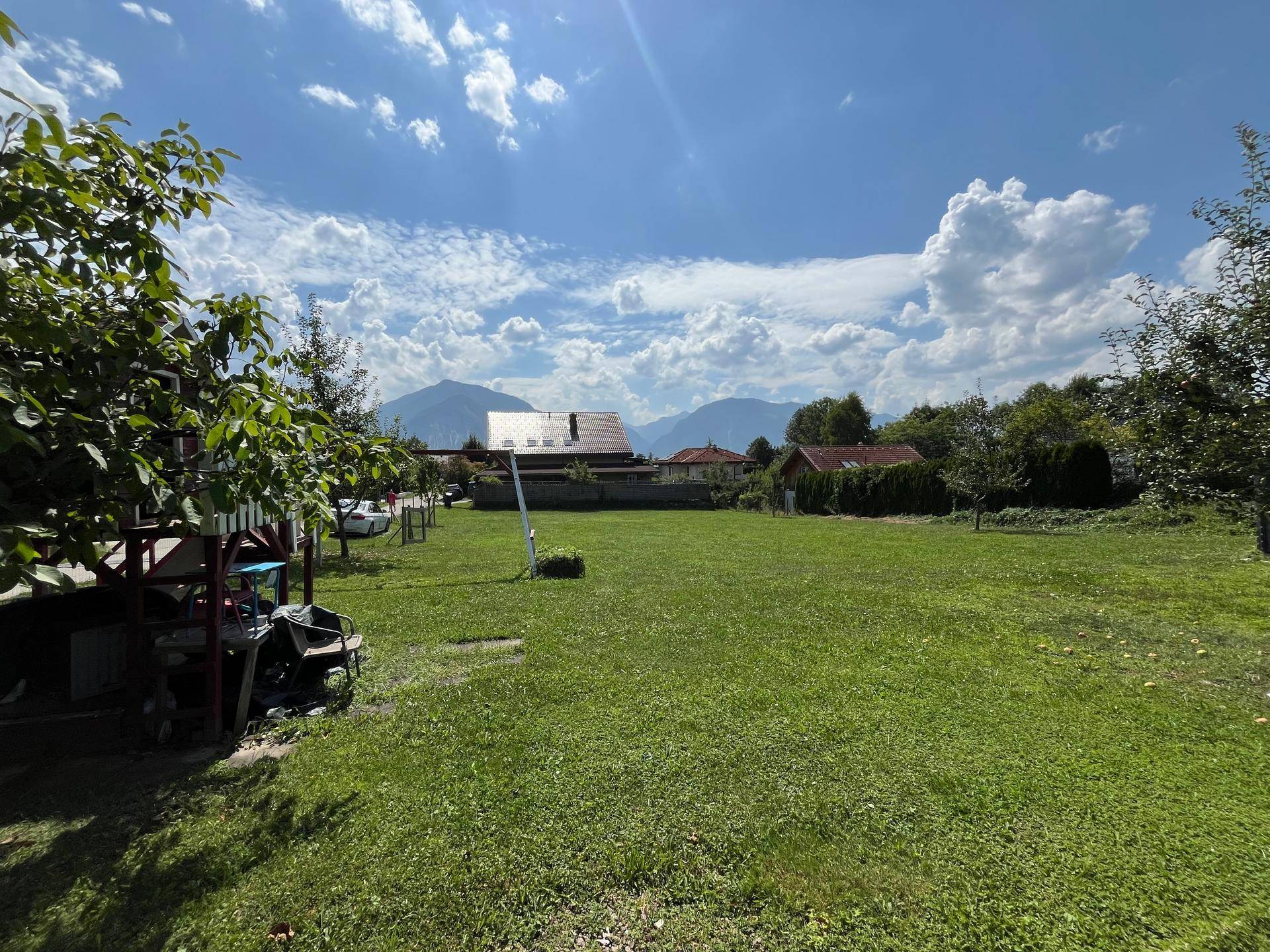 Weitläufiges Gartengrundstück mit grüner Wiese und beeindruckendem Bergblick unter blauem Himmel.