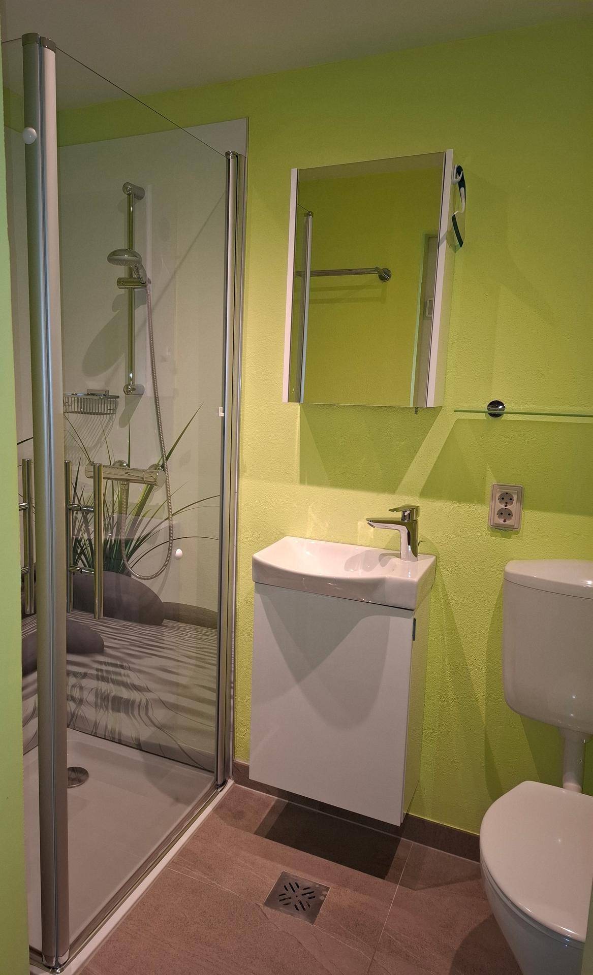 Modernes Badezimmer mit leuchtend grünen Wänden, Duschkabine und weißem Waschbecken.
