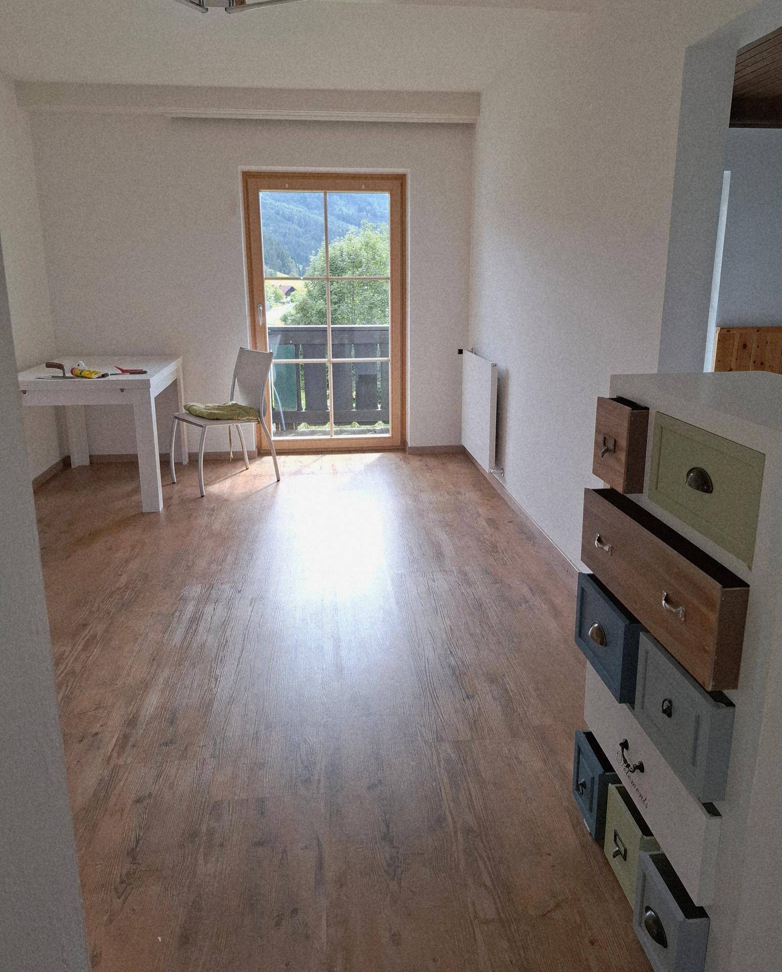 Heller Raum mit Holzboden, großem Fenster und Bergblick, bereit zur individuellen Einrichtung.