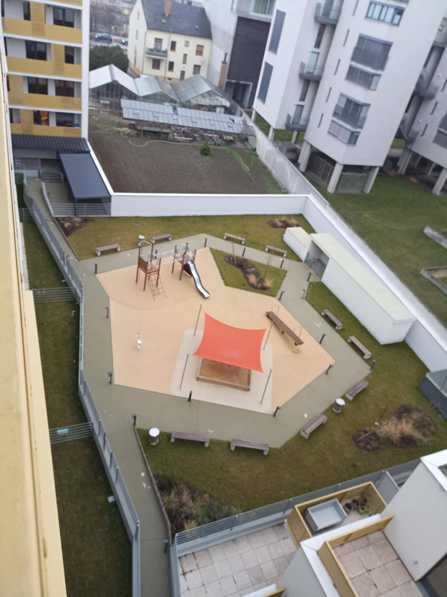 Moderner Kinderspielplatz mit Rutsche, Schaukeln und Sandbereich, umgeben von Grünflächen.