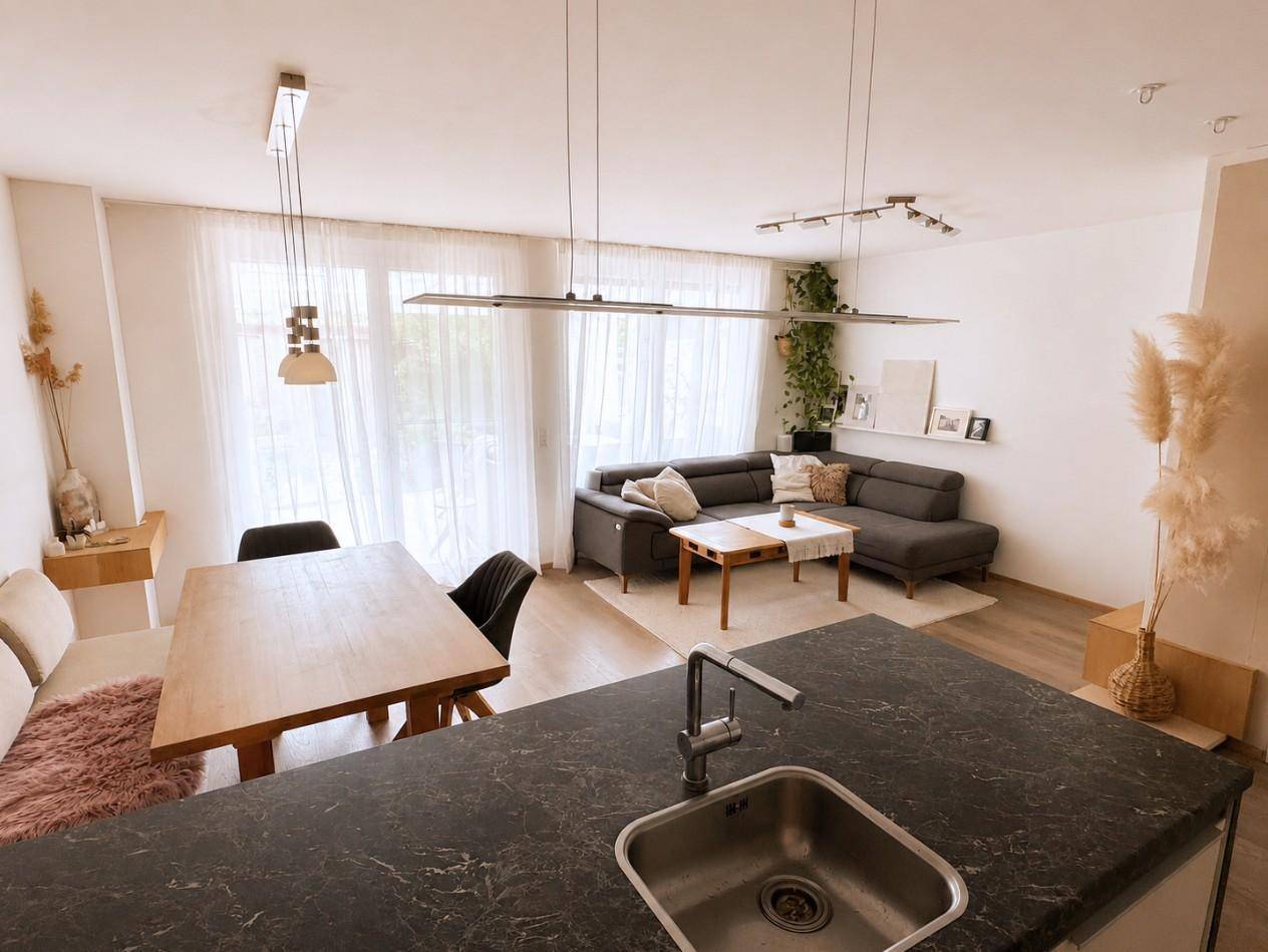 Offener Wohn- und Essbereich mit moderner Einrichtung, großem Fenster und Blick auf die Küche.