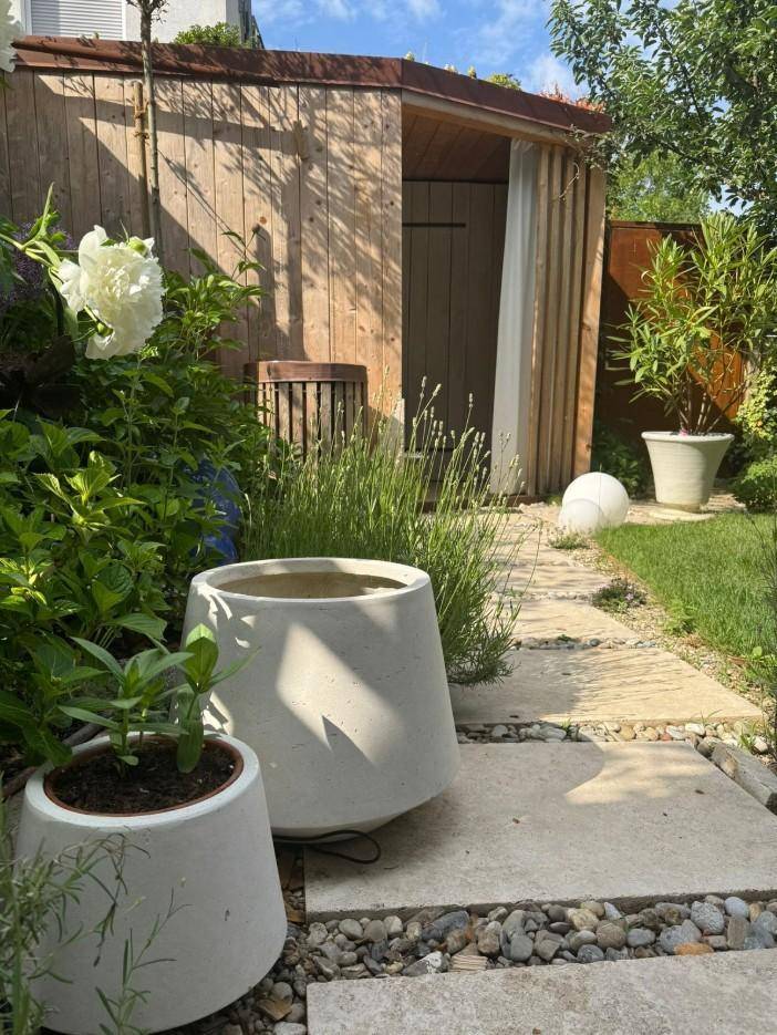 Detailansicht eines Gartenwegs mit Trittsteinen, dekorativen Pflanzen und einem Holzschuppen im Hintergrund.