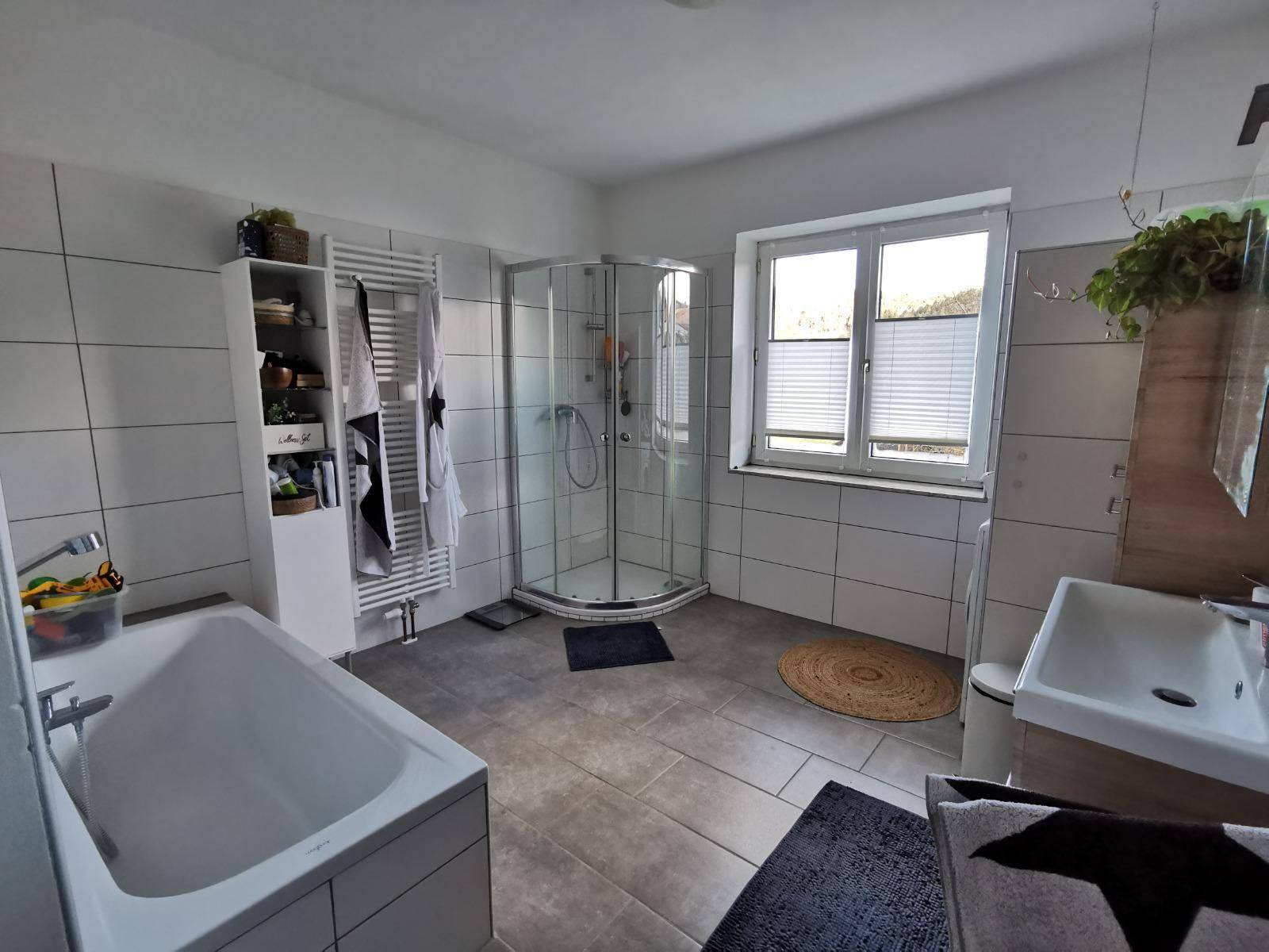 Helles Badezimmer mit Badewanne, Duschkabine, Fenster und Fliesenboden.