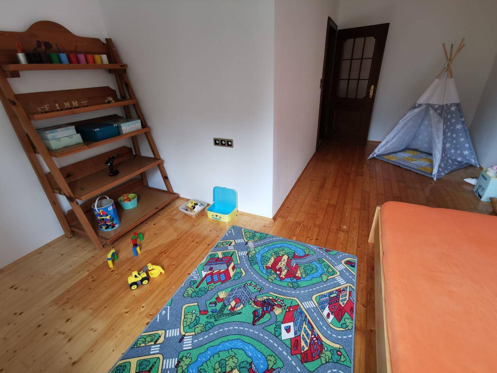 Kinderzimmer mit Holzboden, Spielteppich, Holzregal und Spielzeug.