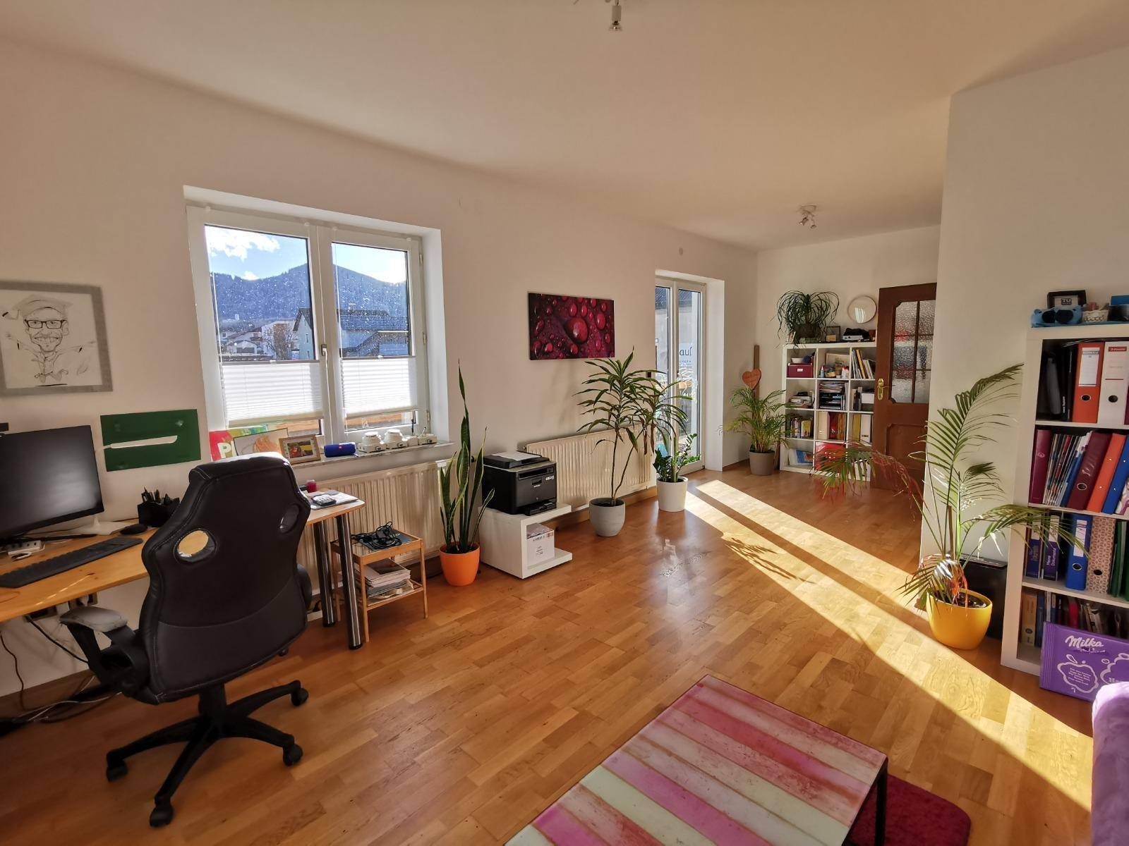 Helles Arbeitszimmer mit Holzboden, Schreibtisch, Pflanzen und Bergblick.