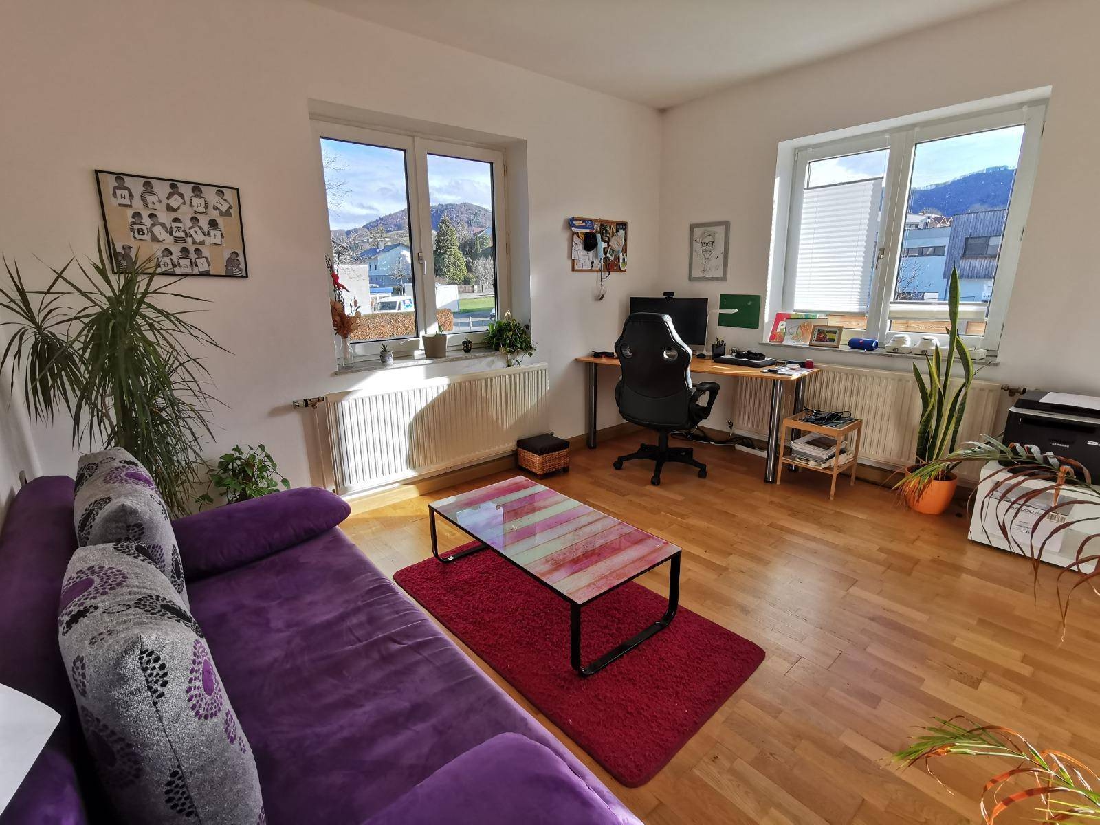Arbeitszimmer mit lila Sofa, Schreibtisch, Holzboden und Bergblick.