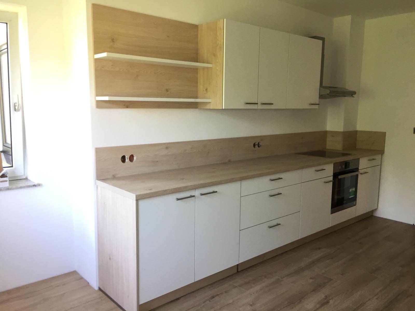 Moderne Einbauküche mit weißen Schränken, Holzarbeitsplatten und integrierten Geräten.