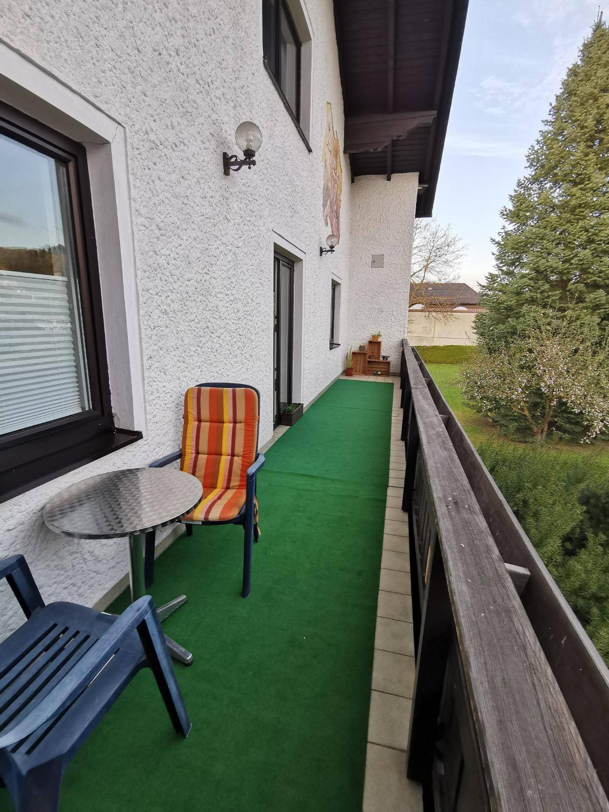 Schmaler Balkon mit Sitzgelegenheiten, Kunstrasen und Blick ins Grüne.