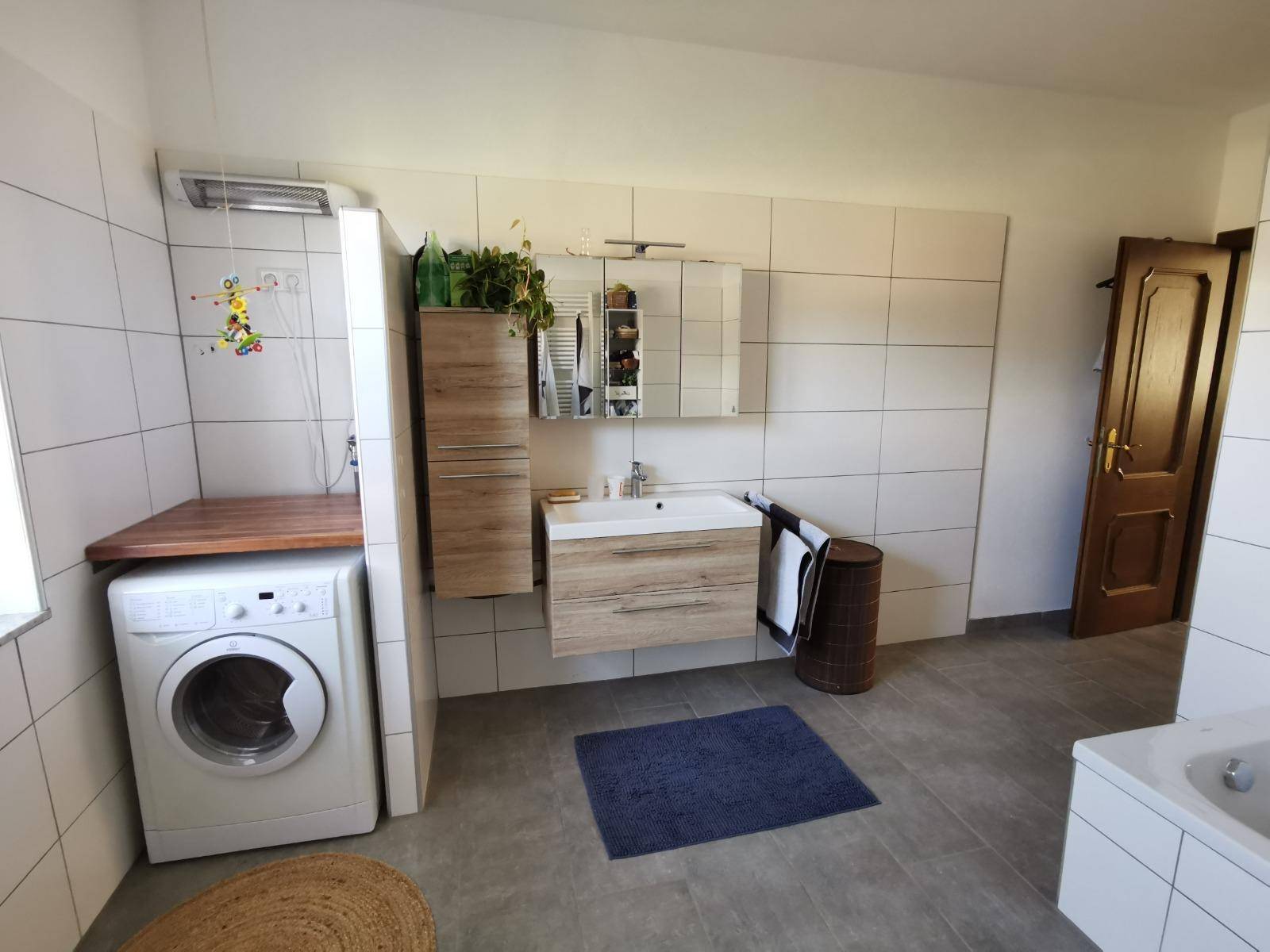 Modernes Badezimmer mit Fliesenboden, Waschmaschine und Holzwaschtisch.