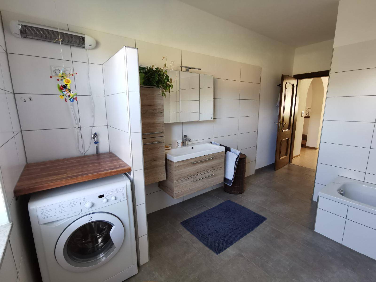 Badezimmer mit Fliesenboden, Waschmaschine, Waschtisch und Spiegelschrank.