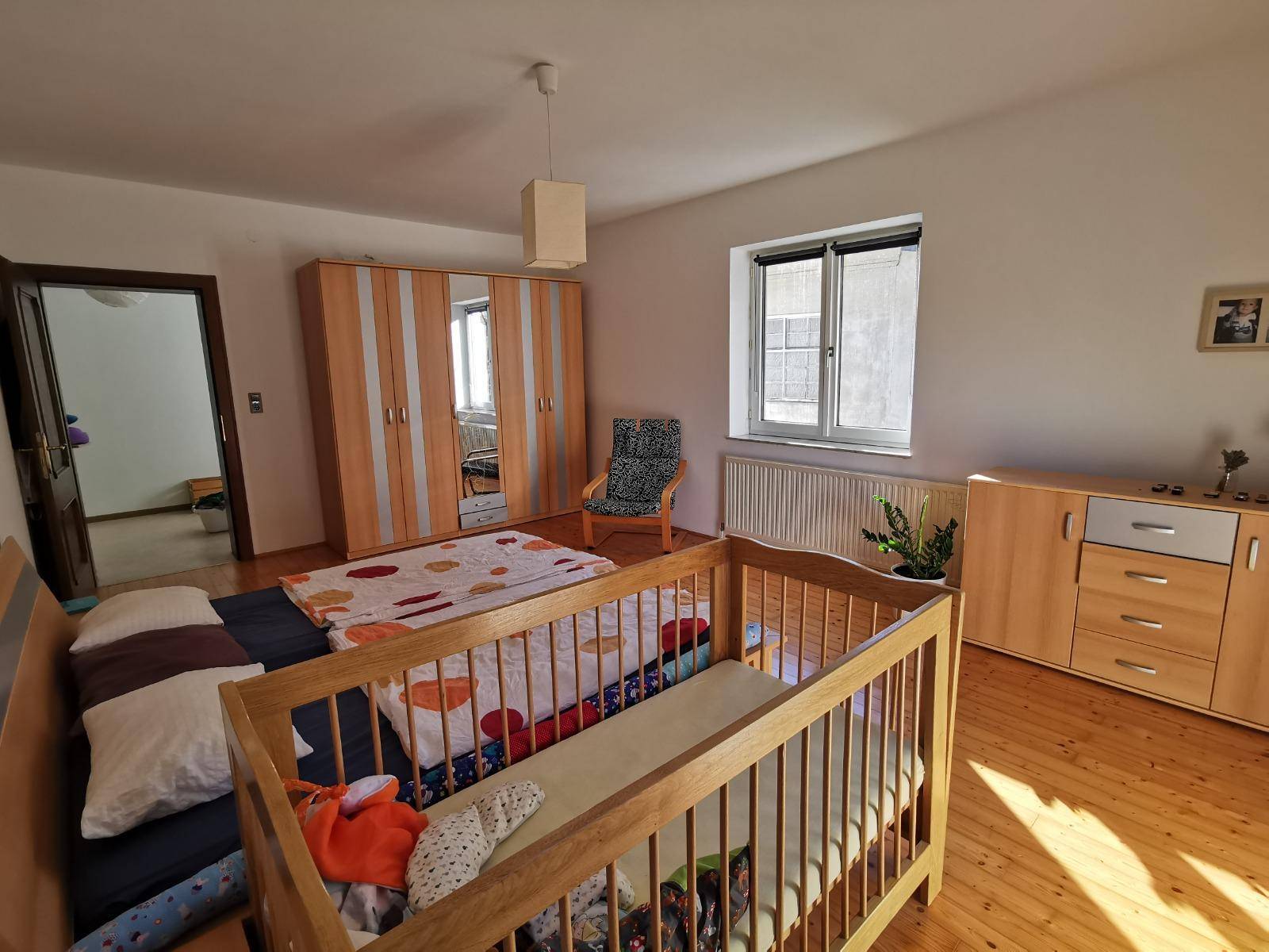 Schlafzimmer mit Holzboden, Doppelbett, Babybett und großem Kleiderschrank.