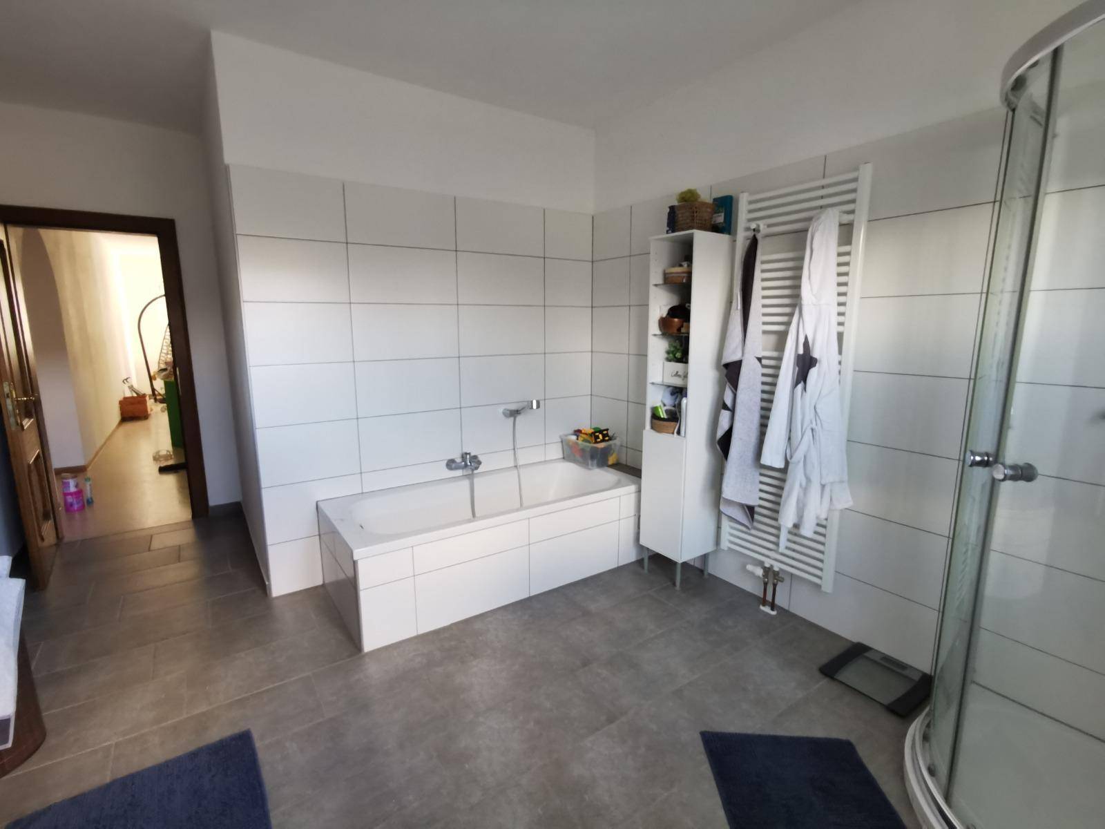 Badezimmer mit Badewanne, Duschkabine, Handtuchheizkörper und Fliesenboden.