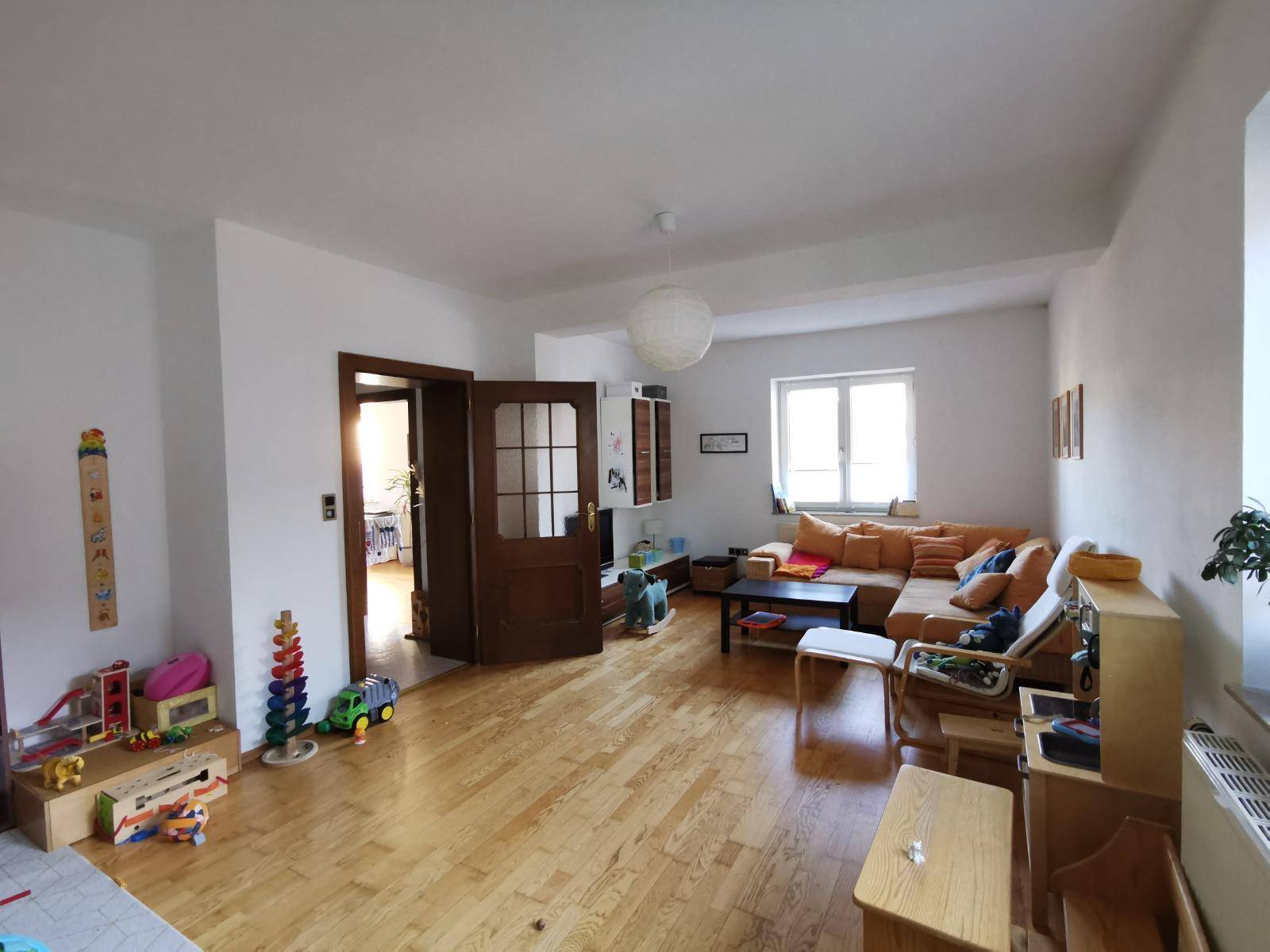 Geräumiges Wohnzimmer mit Holzboden, Kinderspielzeug und einem bequemen Ecksofa.