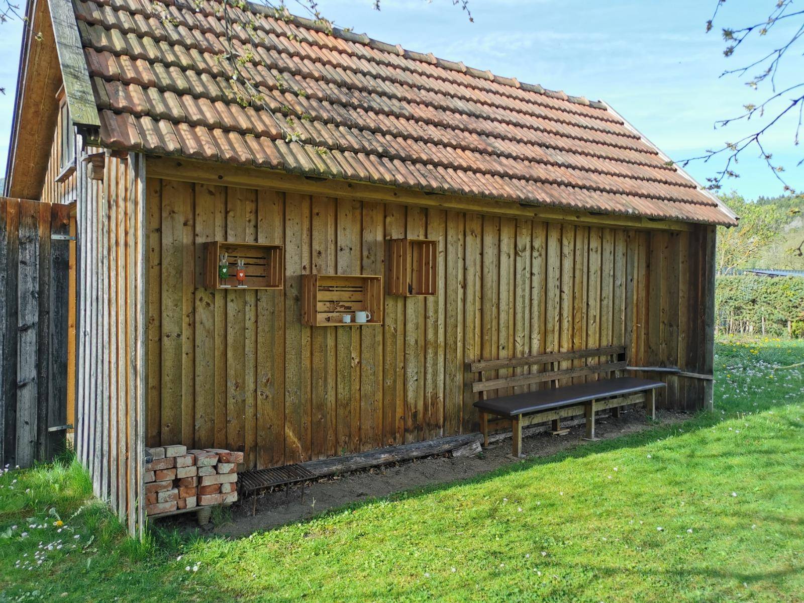 Holzschuppen im Garten mit Sitzbank, Ziegeln und grüner Rasenfläche.