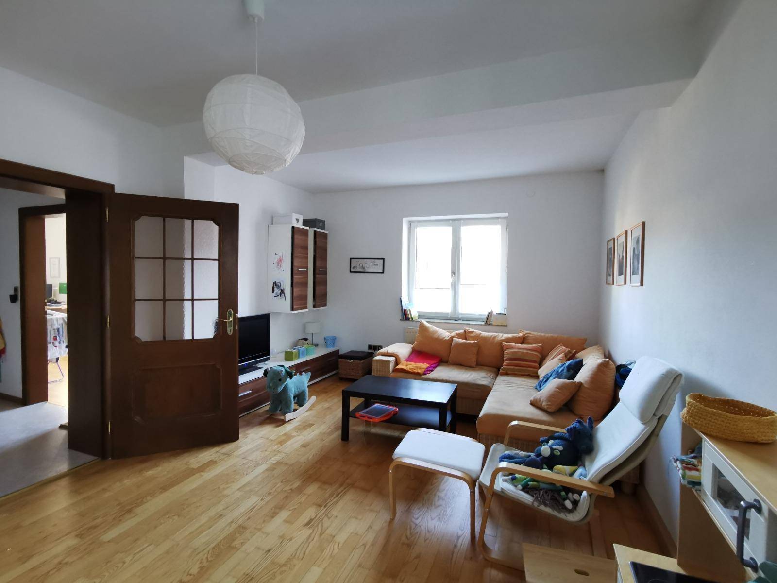 Helles Wohnzimmer mit Holzboden, beigem Ecksofa und einem Fenster.
