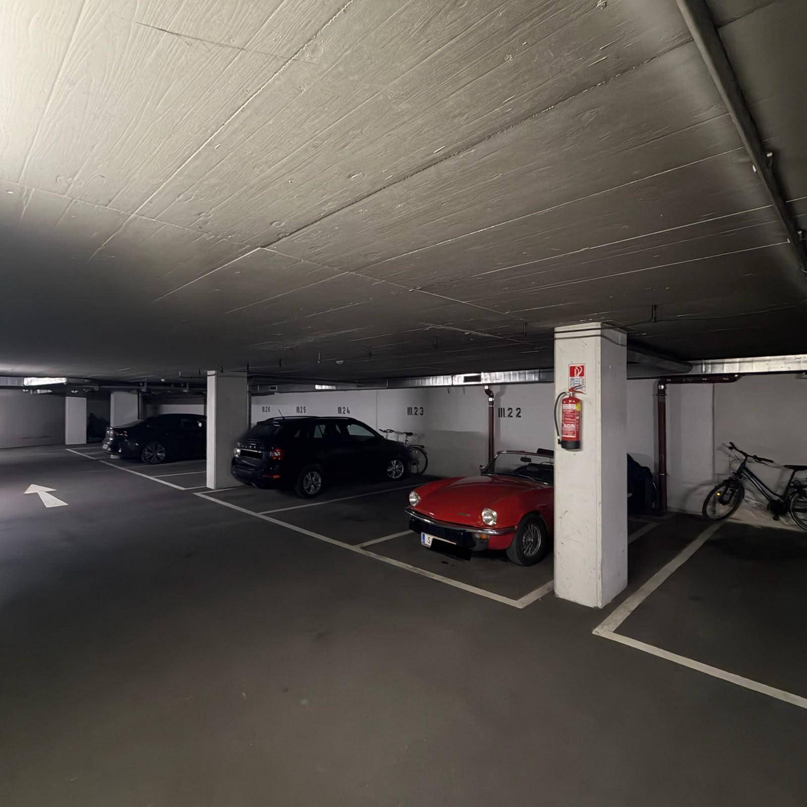 Helle Tiefgarage mit mehreren geparkten Fahrzeugen und einem roten Feuerlöscher an einer Säule.