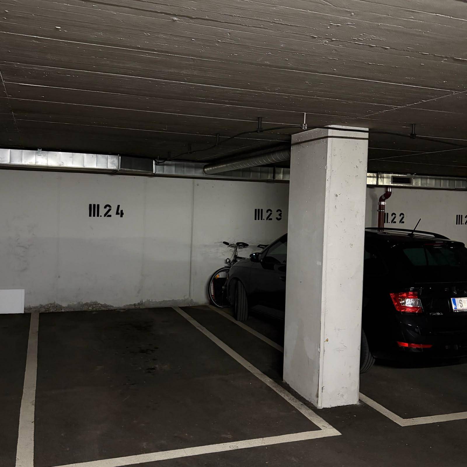 Parkplätze in der Tiefgarage mit einem geparkten Auto und einem Fahrrad an der Wand.