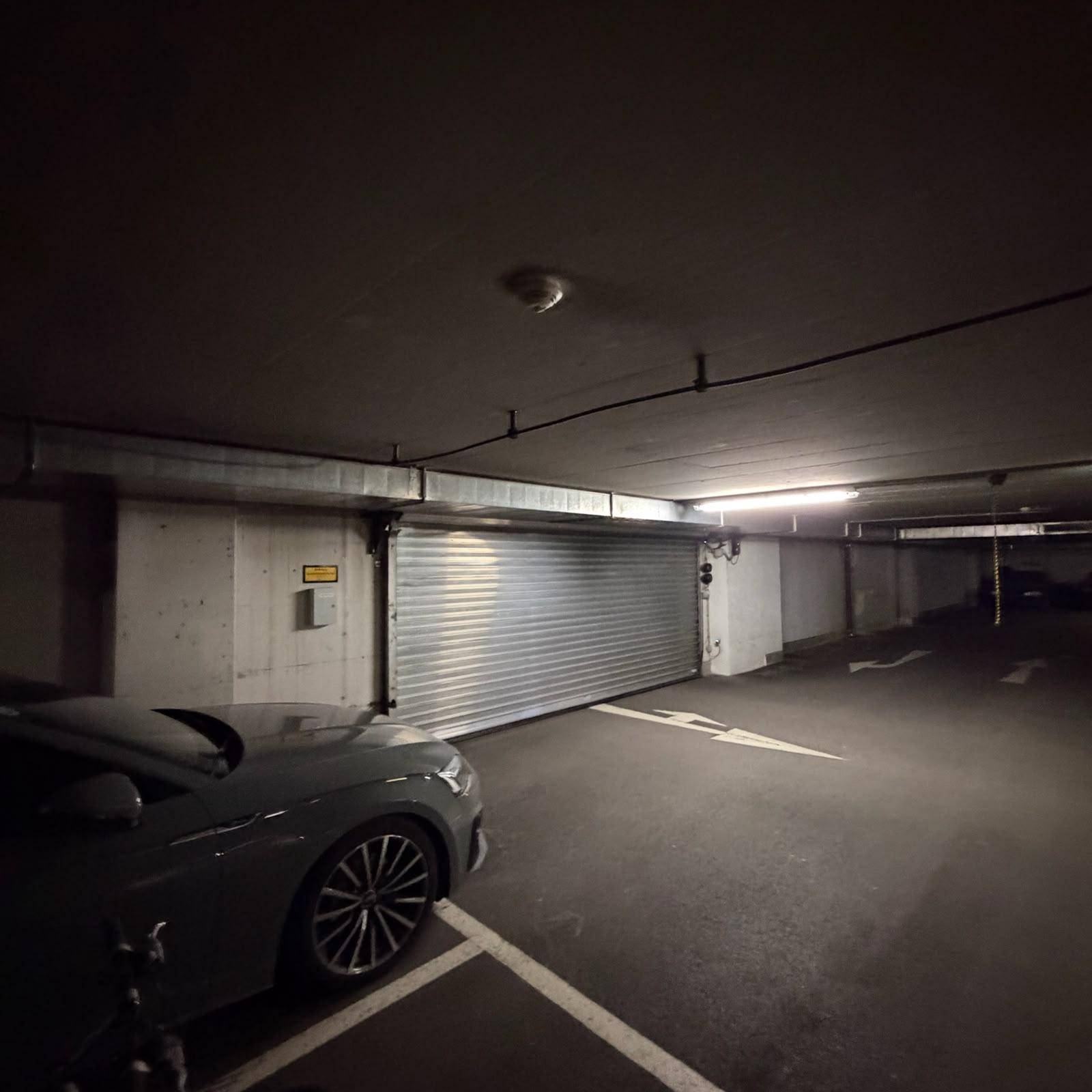 Einfahrt zur Tiefgarage mit einem geschlossenen Rolltor und einem geparkten Auto im Vordergrund.