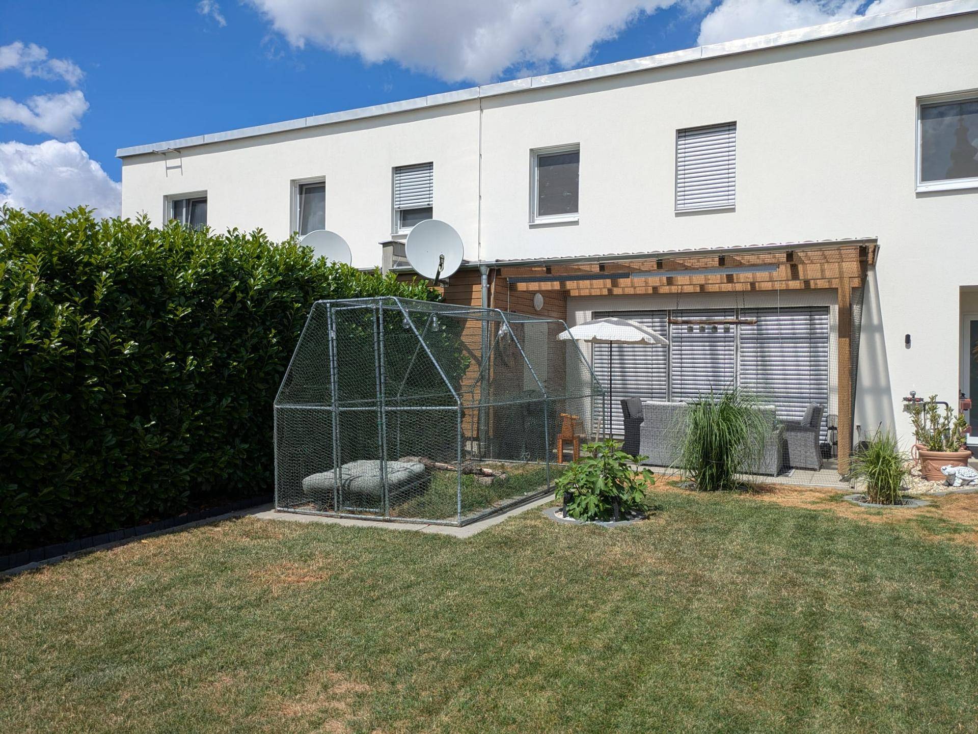 Hinterhof mit Rasenfläche, überdachter Terrasse und einem großen Tiergehege.