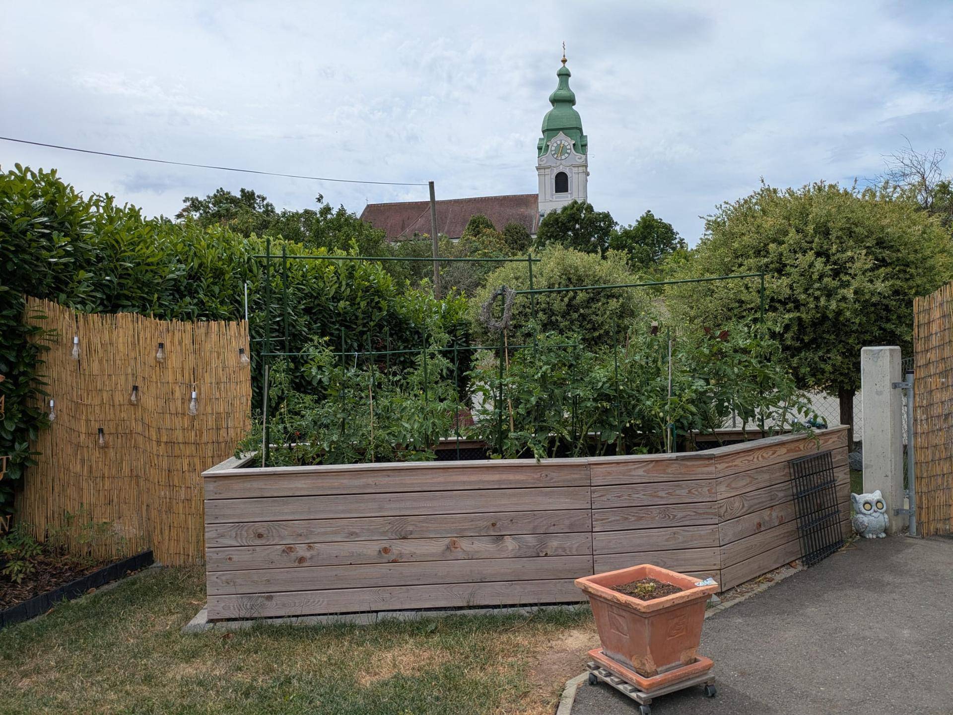 Erhöhtes Gemüsebeet im Garten mit Bambuszaun und Blick auf die Kirche.