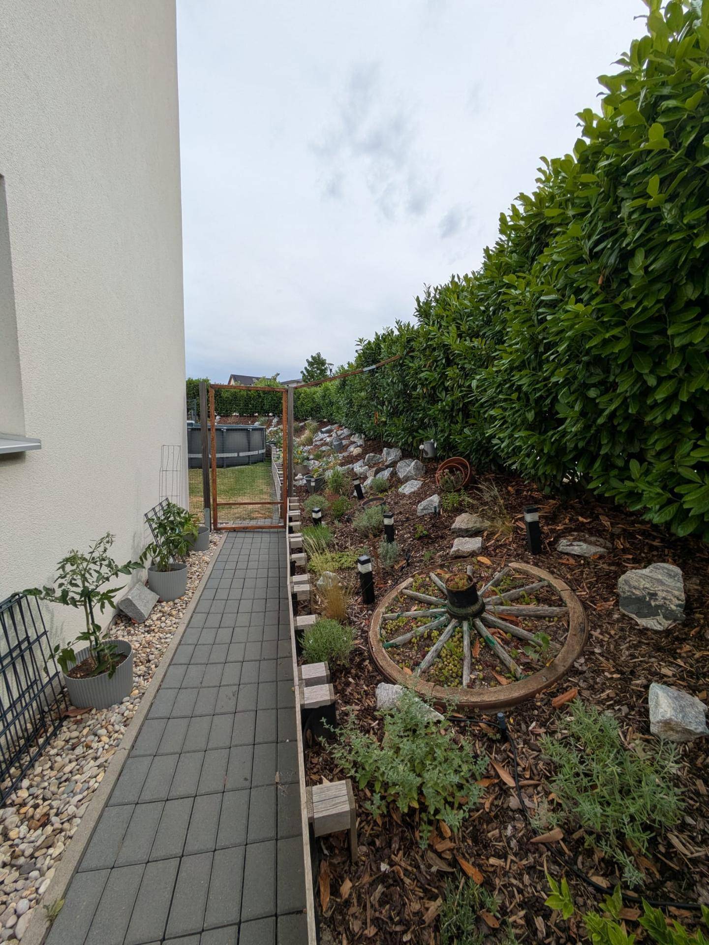 Seitlicher Gartenweg mit gepflastertem Pfad und einem dekorativen Blumenbeet.