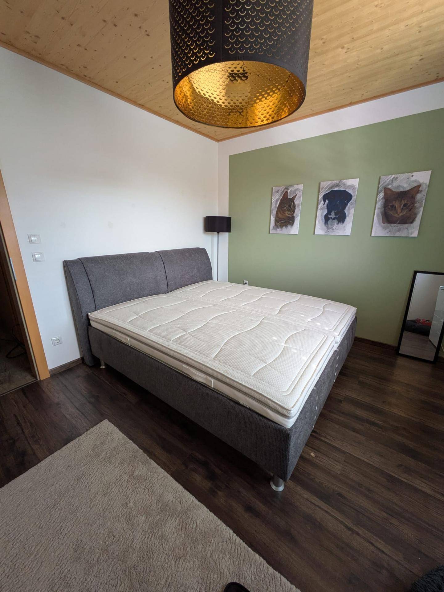 Schlafzimmer mit Doppelbett, grüner Akzentwand und Holzdecke.