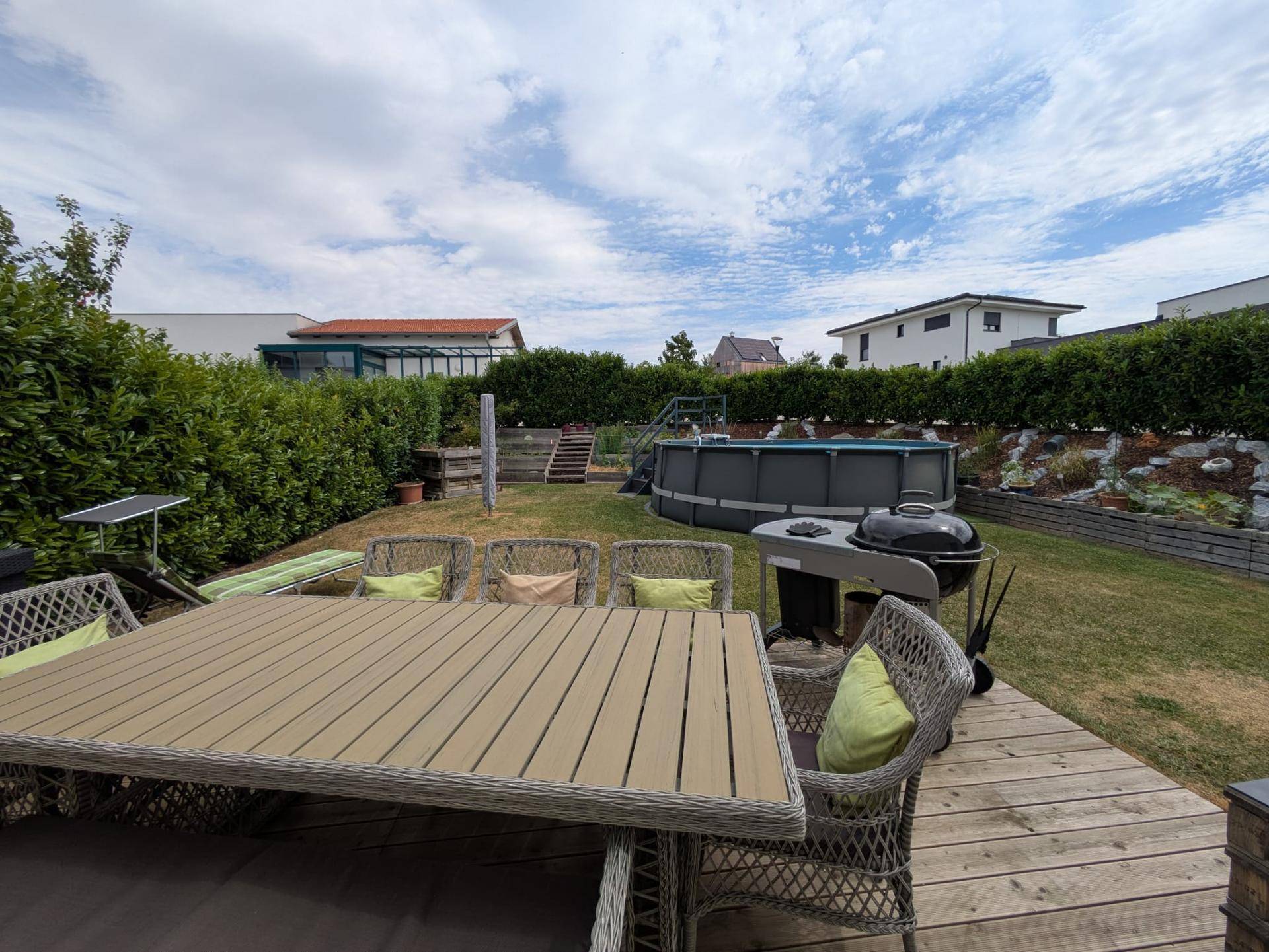 Gartenbereich mit Esstisch auf Holzdeck, Grill und Aufstellpool im Hintergrund.